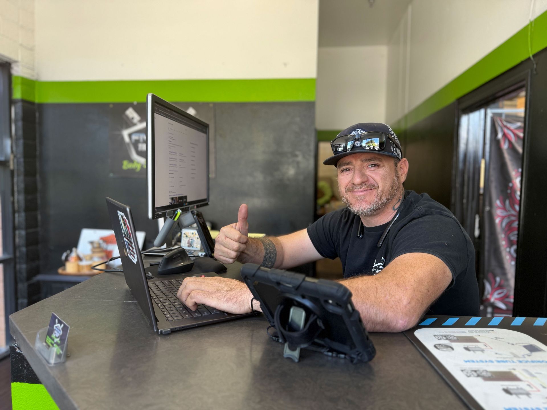 Man at desk with laptop, giving thumbs up. Office setting with black and green accents.