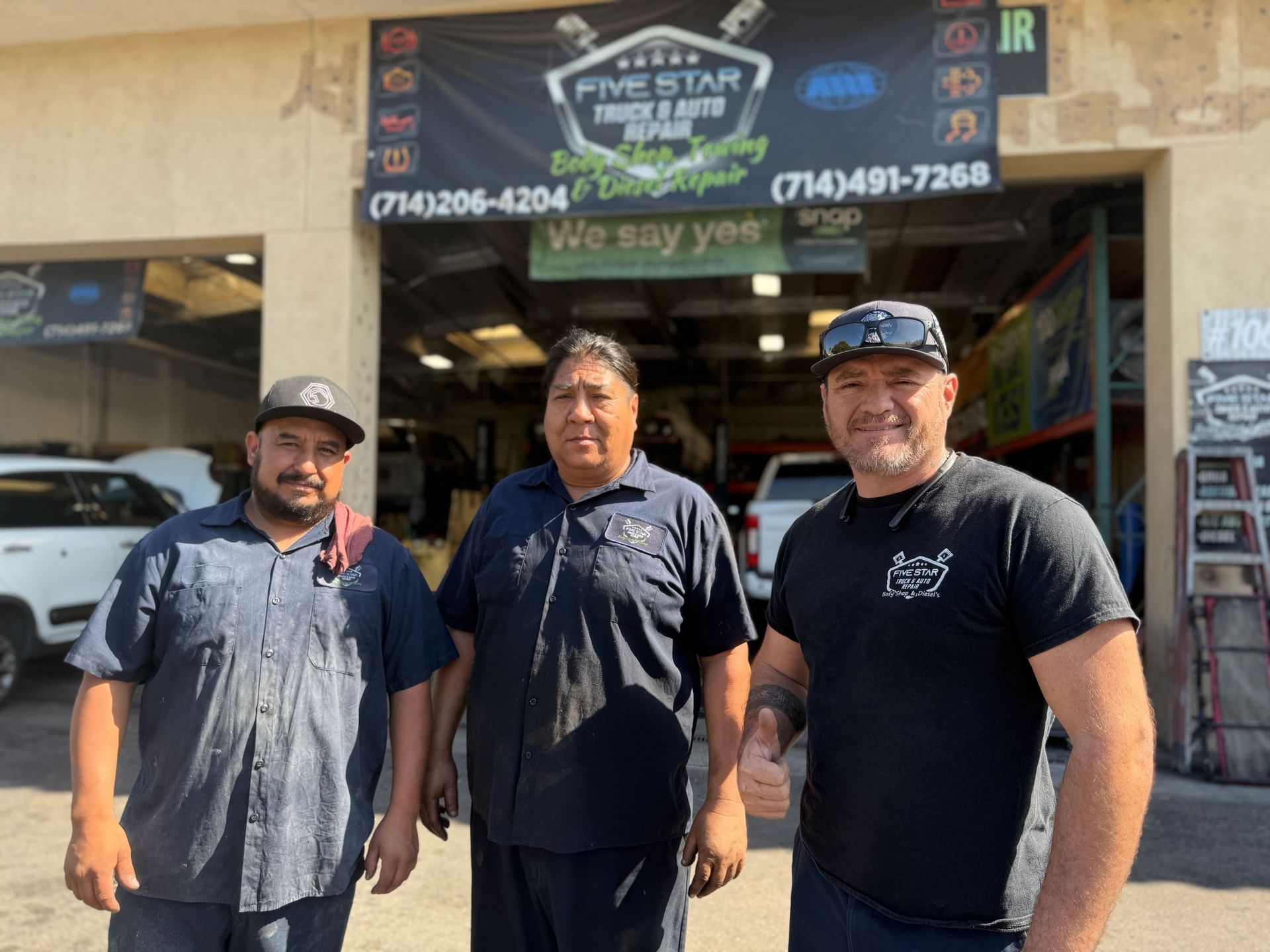 Three men standing in front of an auto repair shop. They are smiling, and the shop sign says 