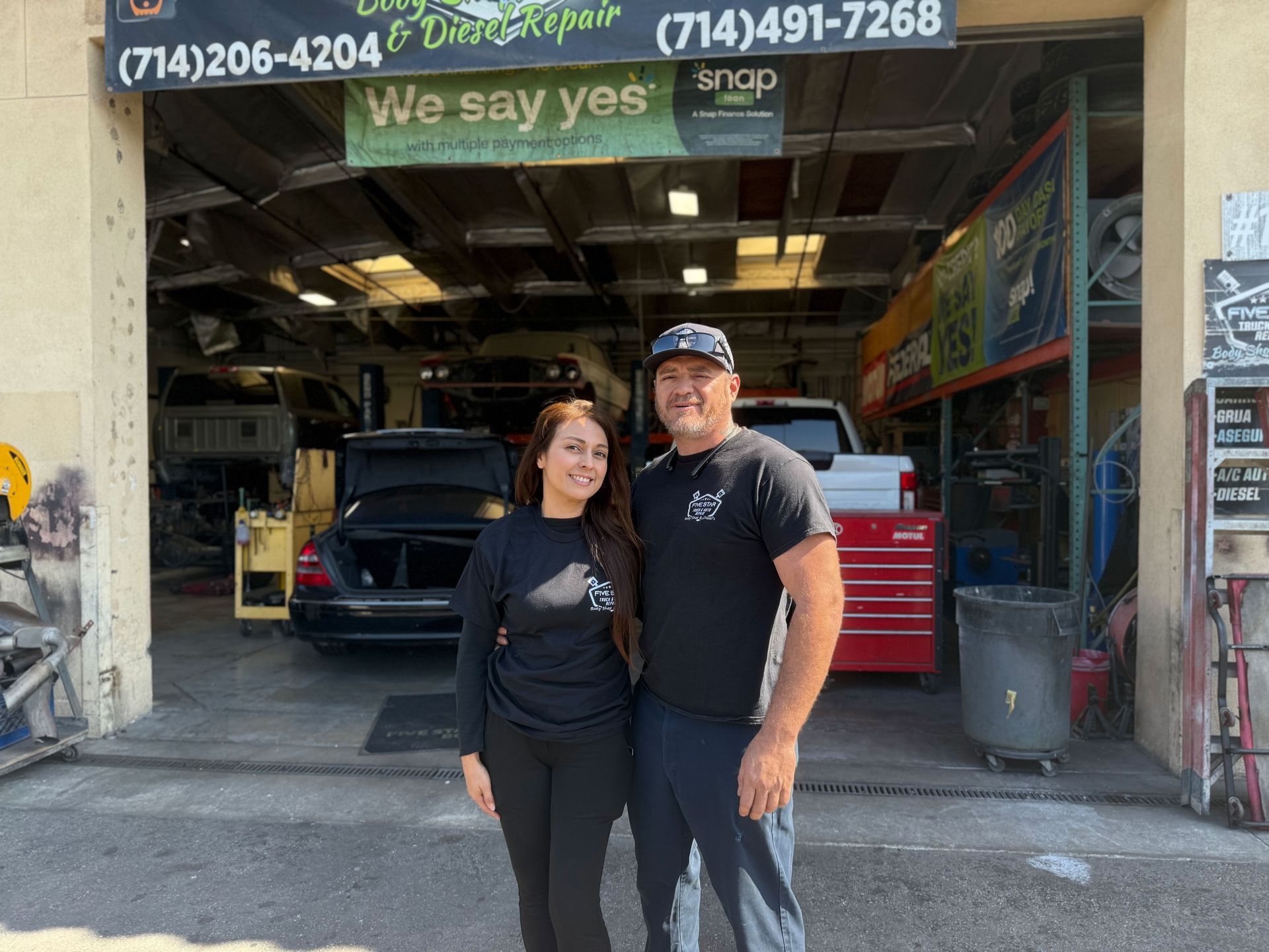 Two people, a woman and a man, standing outside a car repair shop.