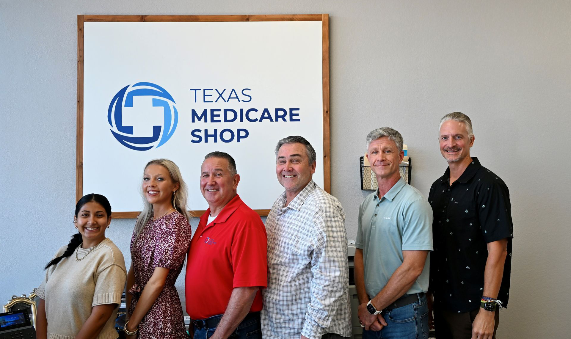 Texas Medicare Shop staff posing beside company sign in an office.