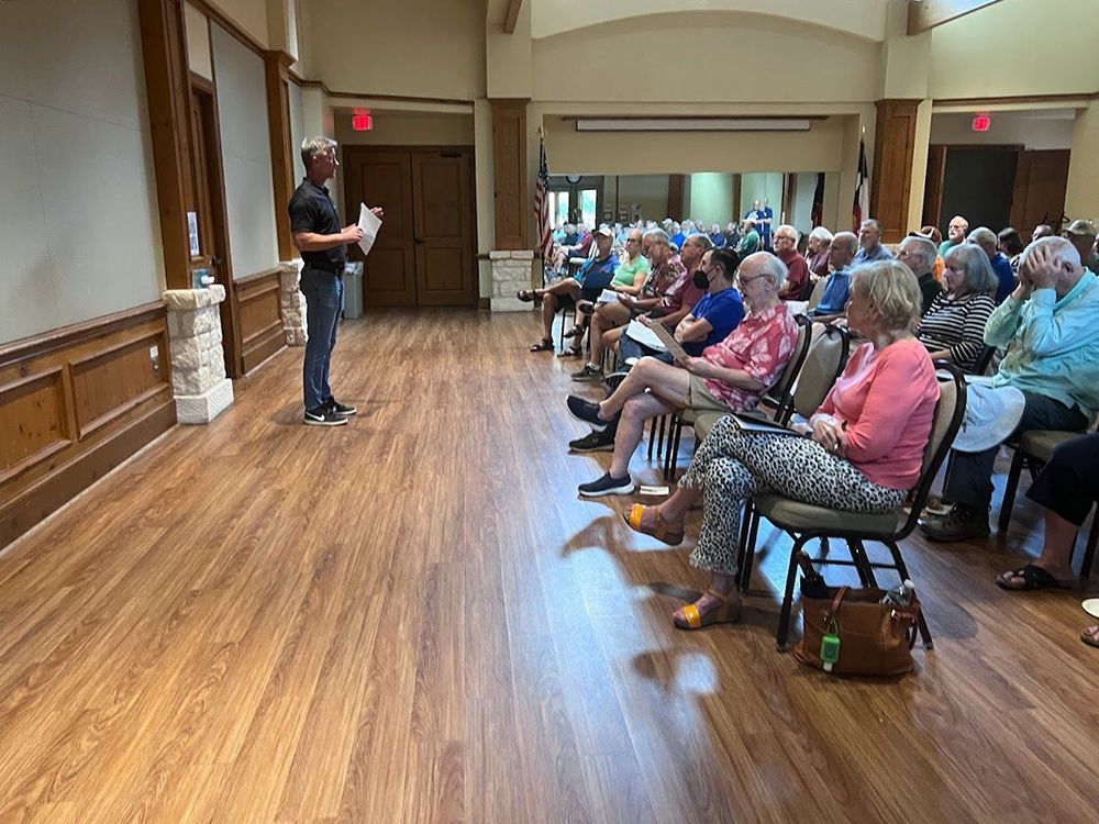A man is standing in front of a large group of people sitting in chairs.