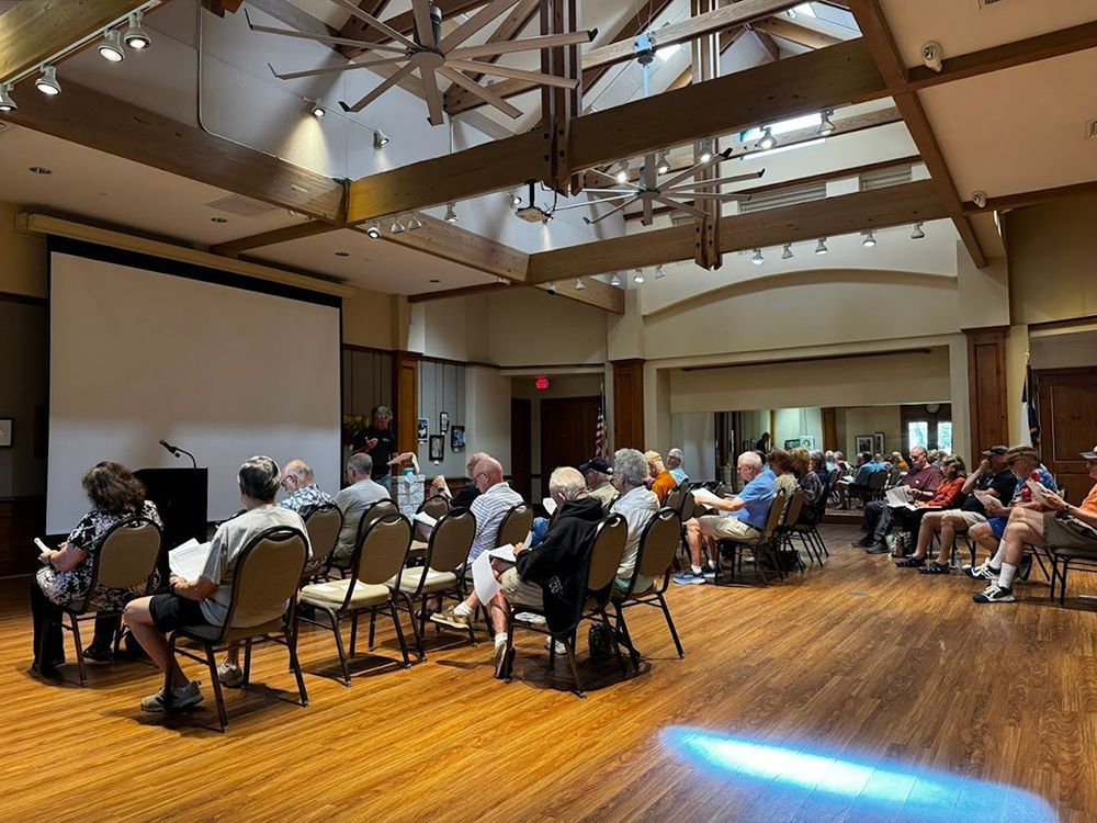 A group of people are sitting in chairs in front of a large screen in a large room.
