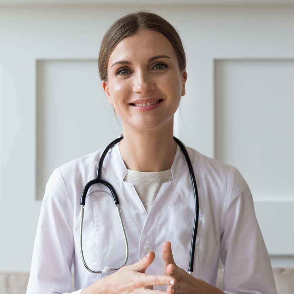 A female doctor with a stethoscope around her neck is smiling at the camera.