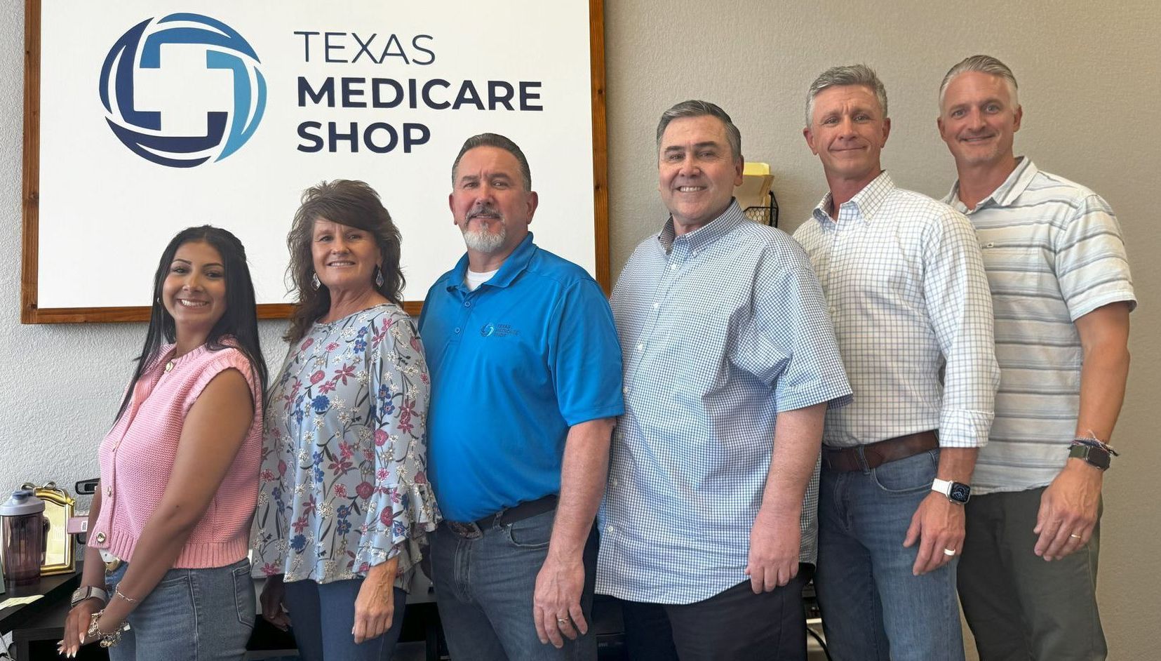 A group of people are posing for a picture in front of a sign for the texas medicare shop.