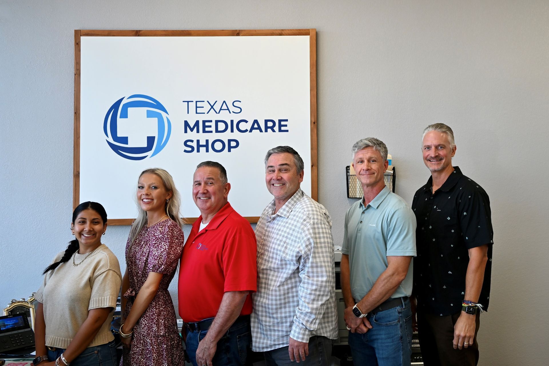 Six people posing beside a Texas Medicare Shop sign in an office.