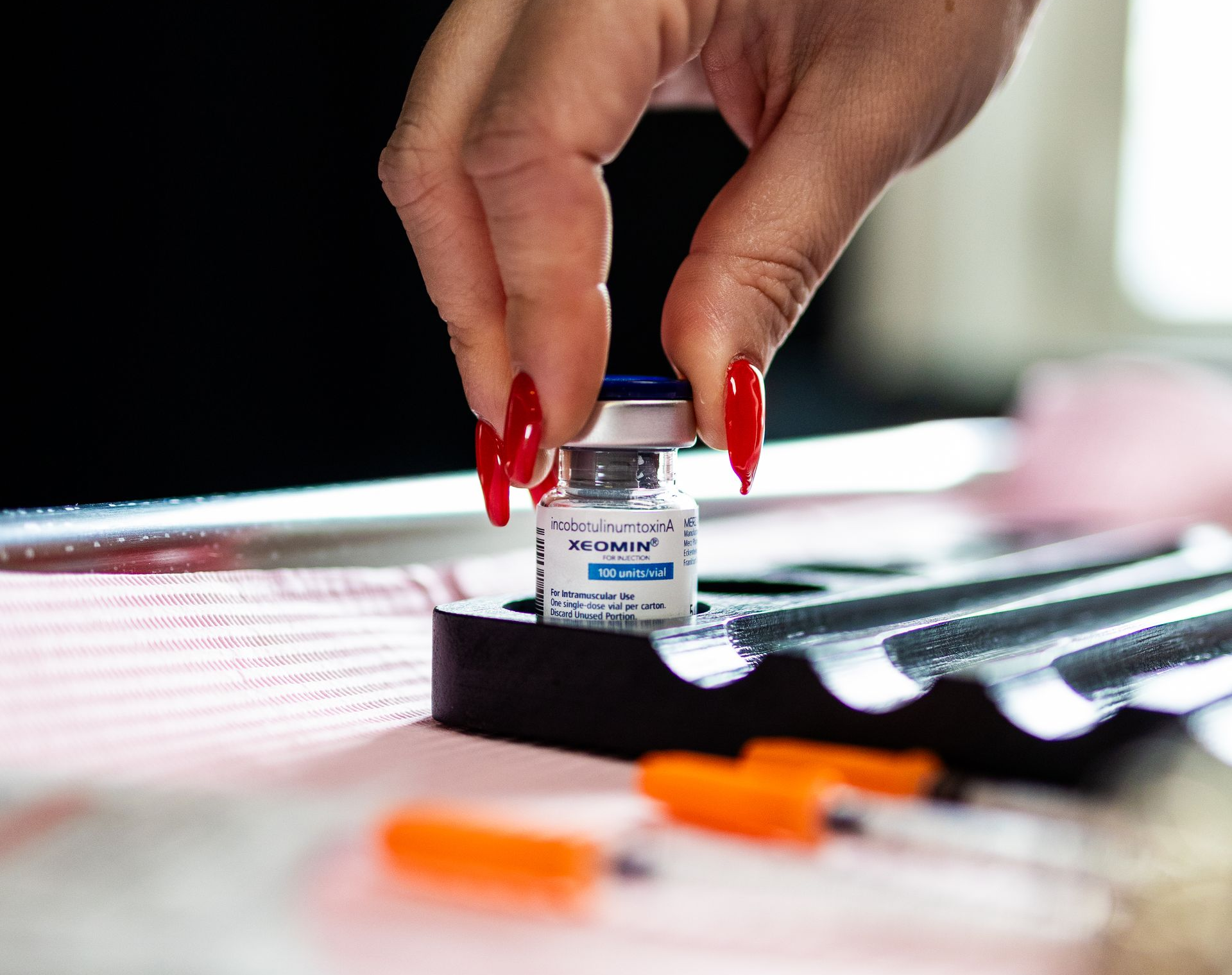 Hand placing a small vaccine vial beside a syringe on a medical tray