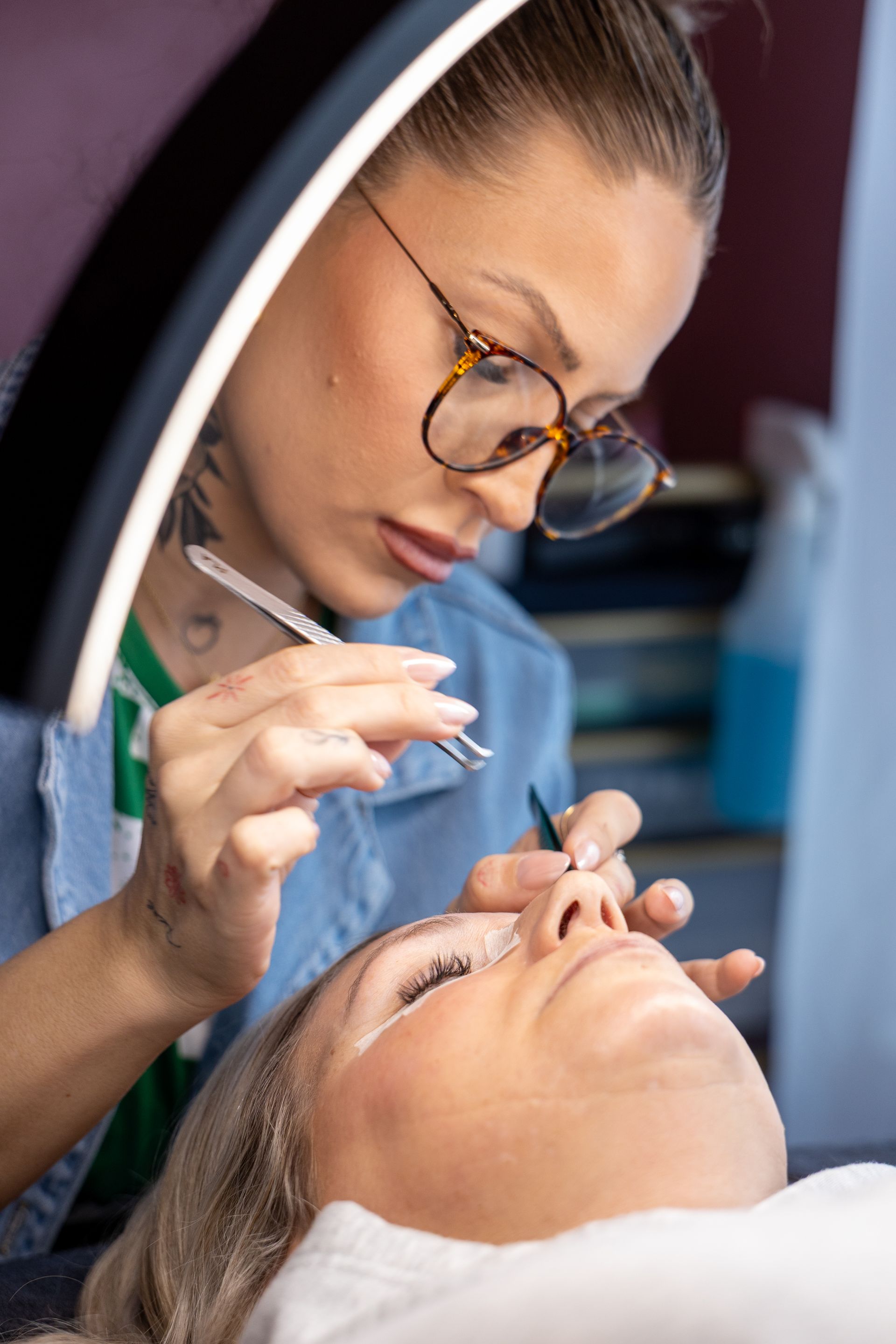 Close-up of a beautician applying treatment to a client’s eyebrows under a ring light