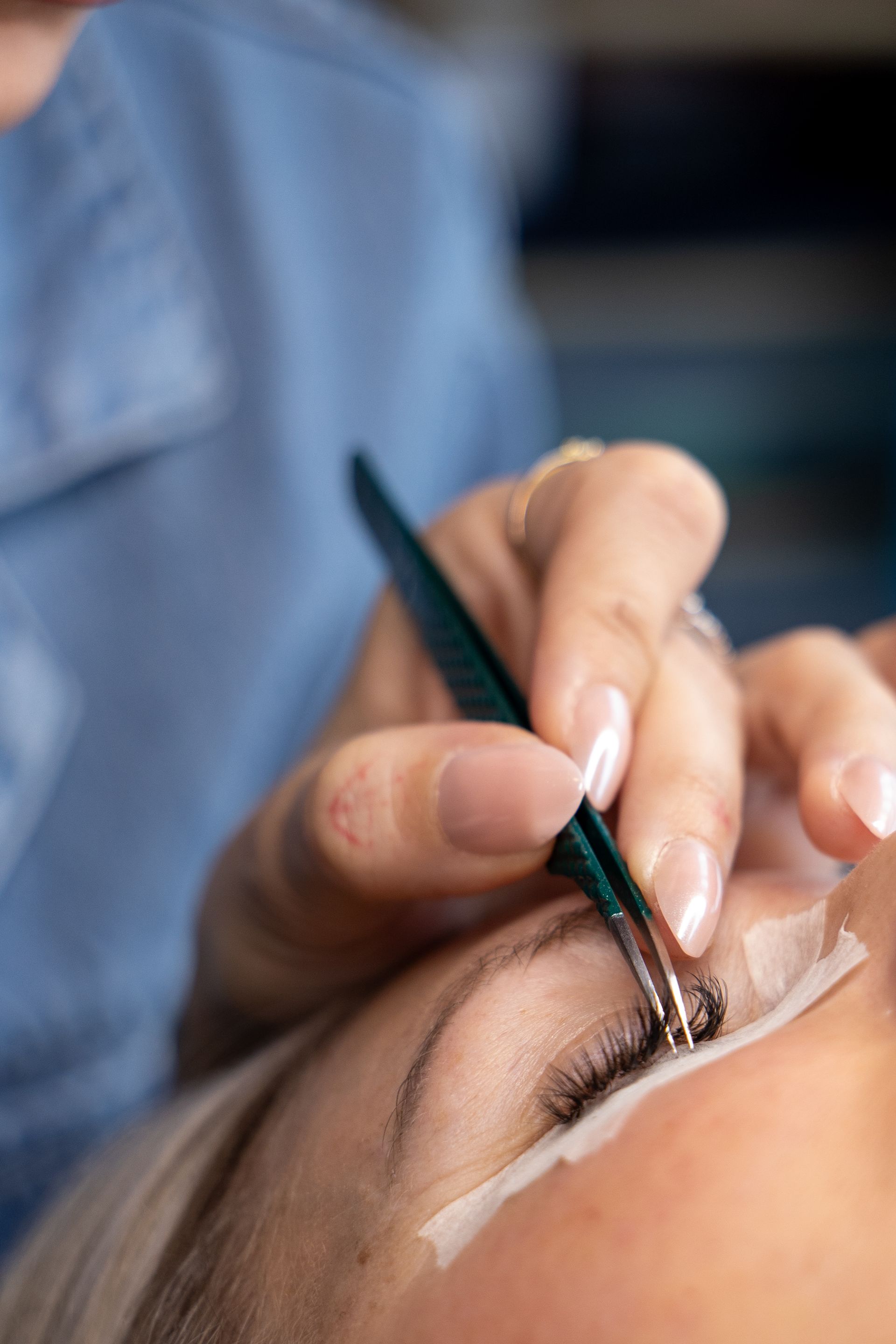 Beauty technician applying eyelash extensions to a client’s closed eye with a small brush.