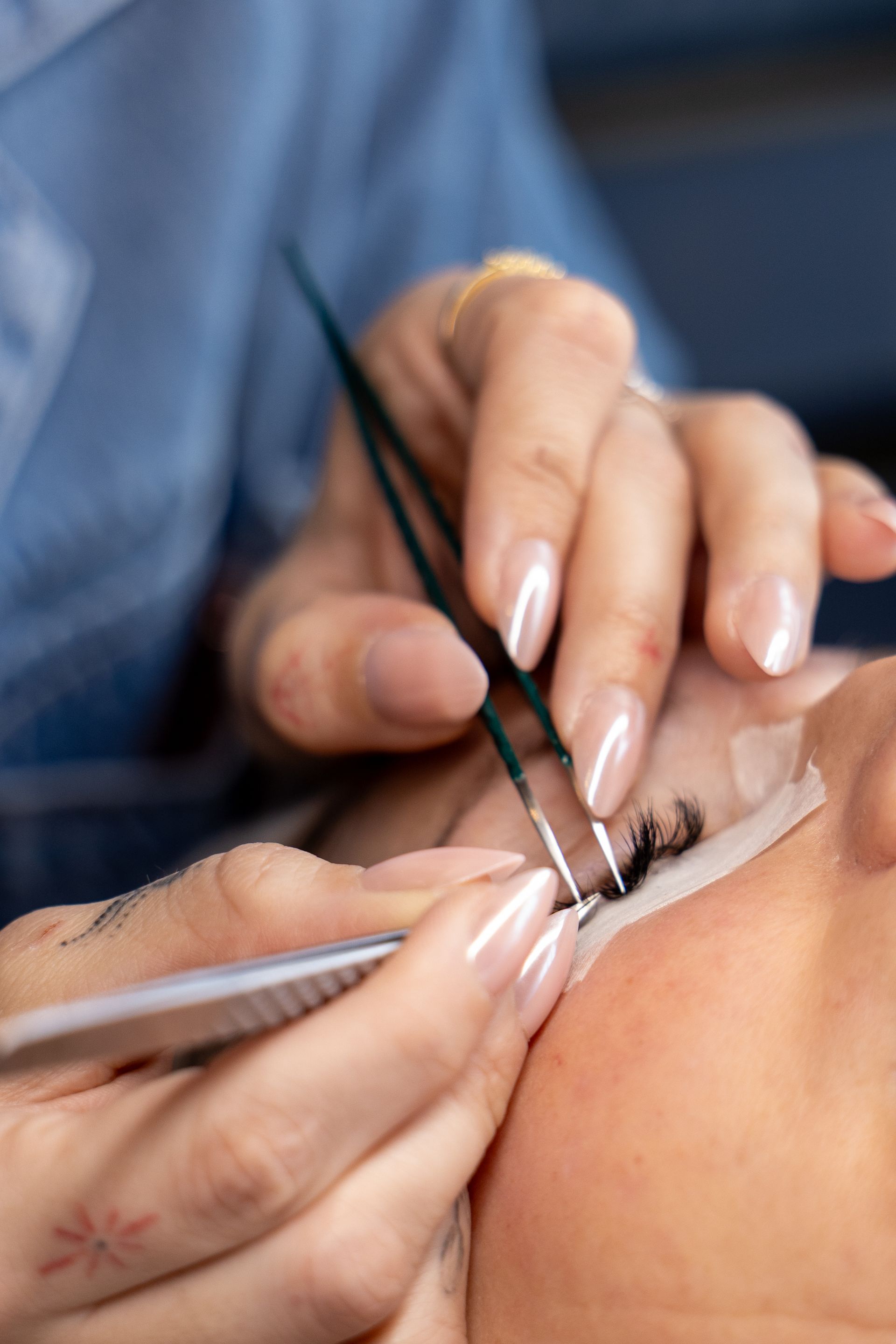 Hands applying eyelash extensions with tweezers in a close-up beauty treatment.