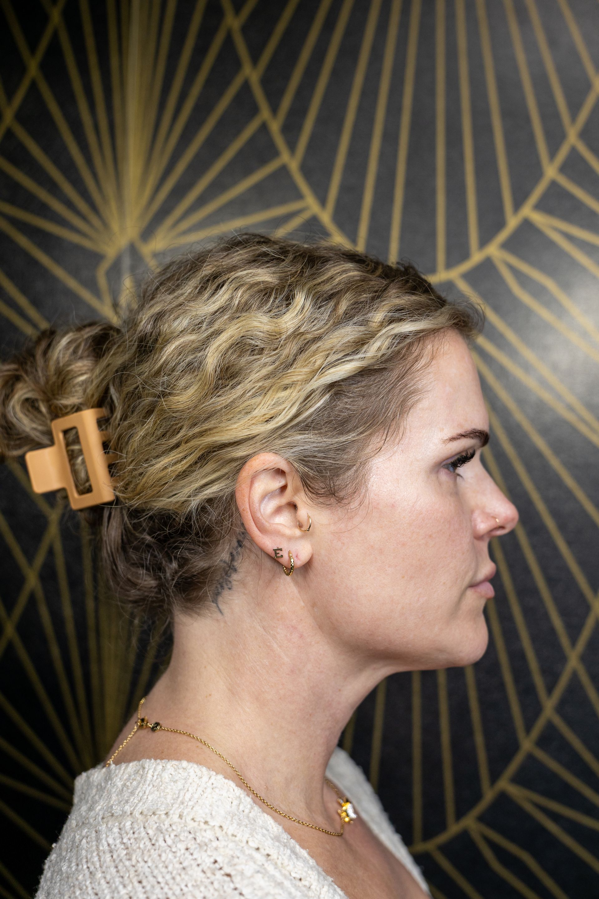 Profile view of a woman with blonde hair in a gold clip against a dark geometric background