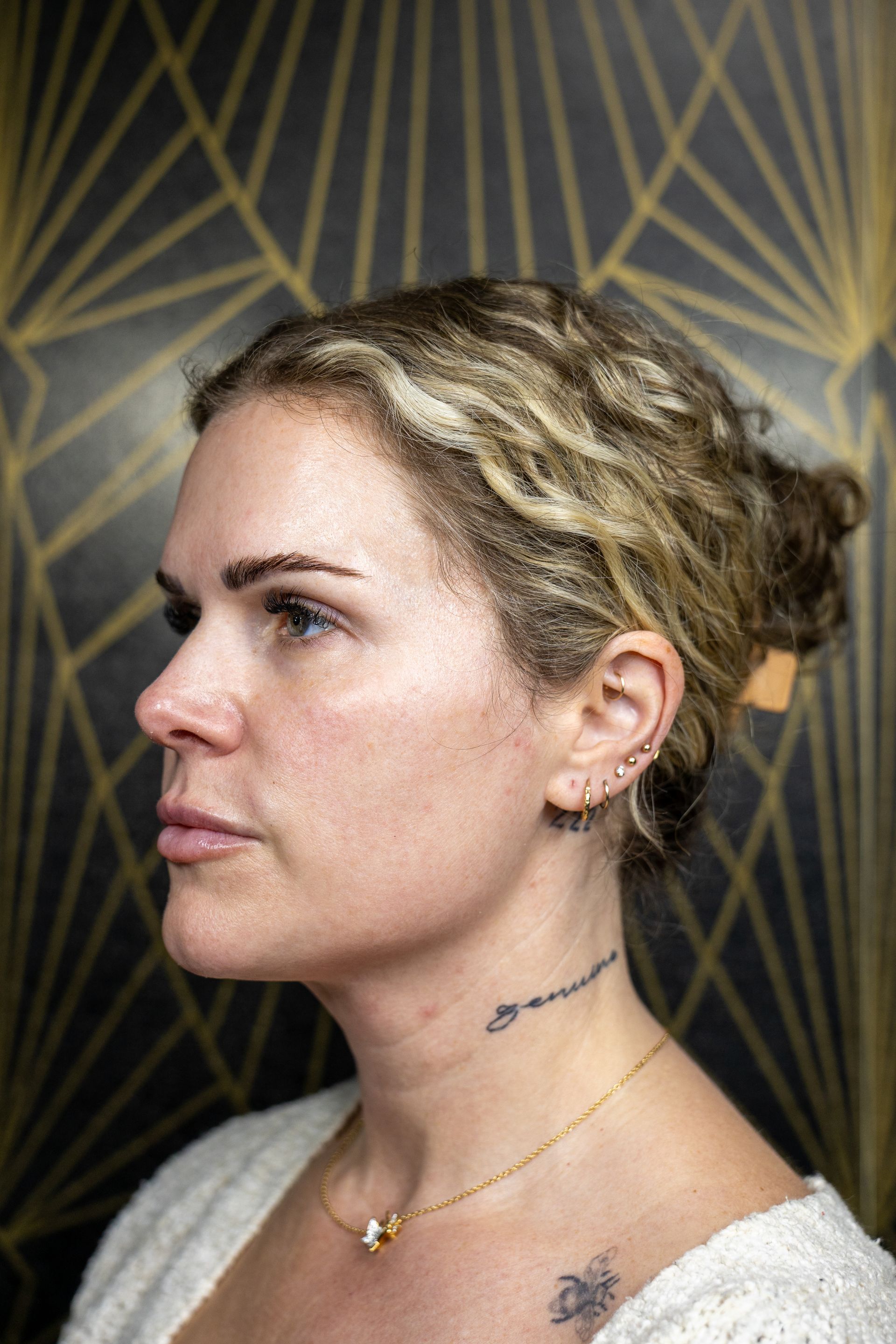 Side-profile portrait of a braided blonde person against a dark geometric wall.