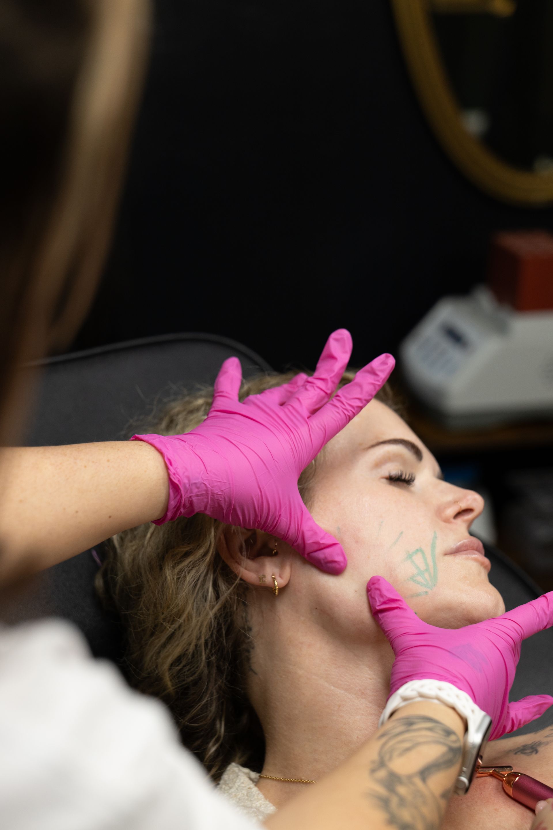 A person receives a facial treatment as a gloved aesthetician applies product to their face.