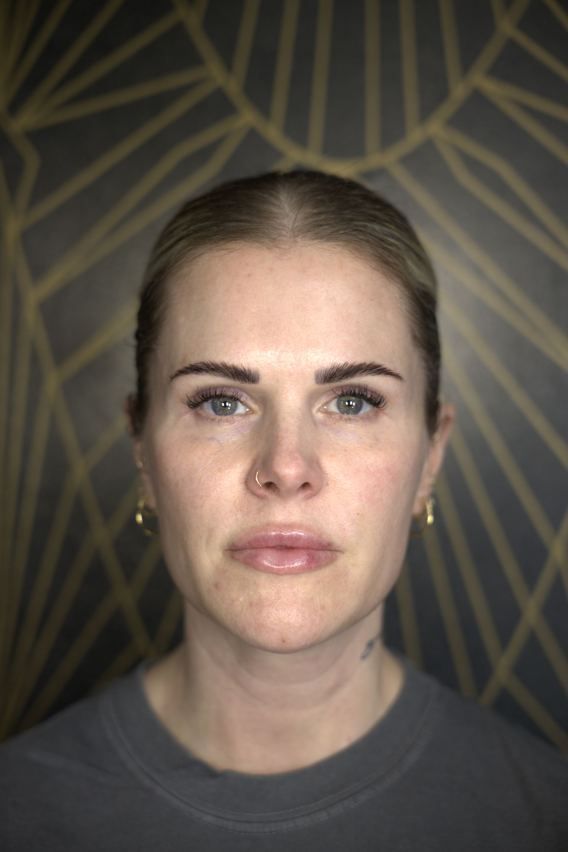 Portrait of a woman against a dark geometric background, facing forward with a neutral expression