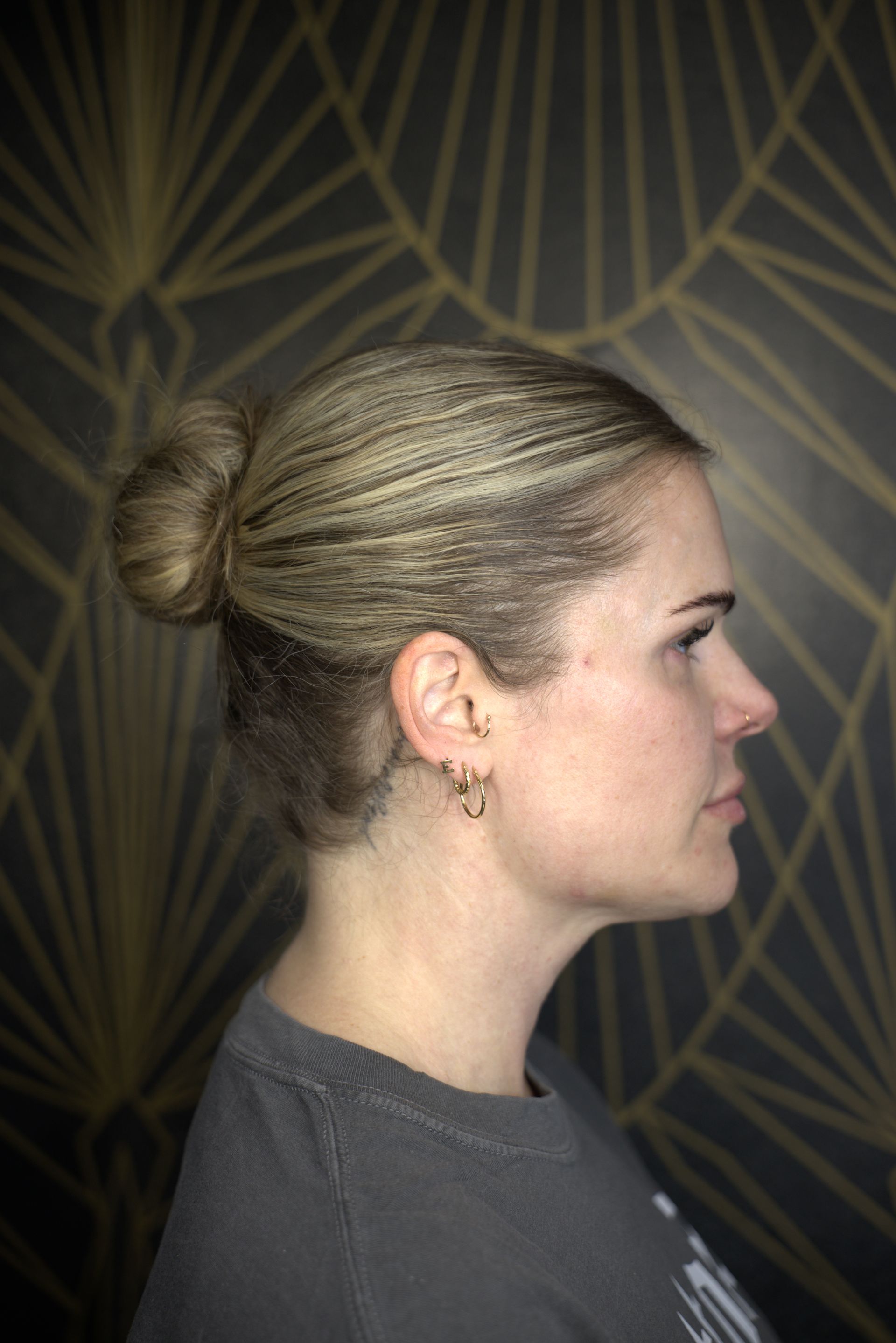 Profile view of a woman with blonde hair in a bun against a dark geometric-patterned background