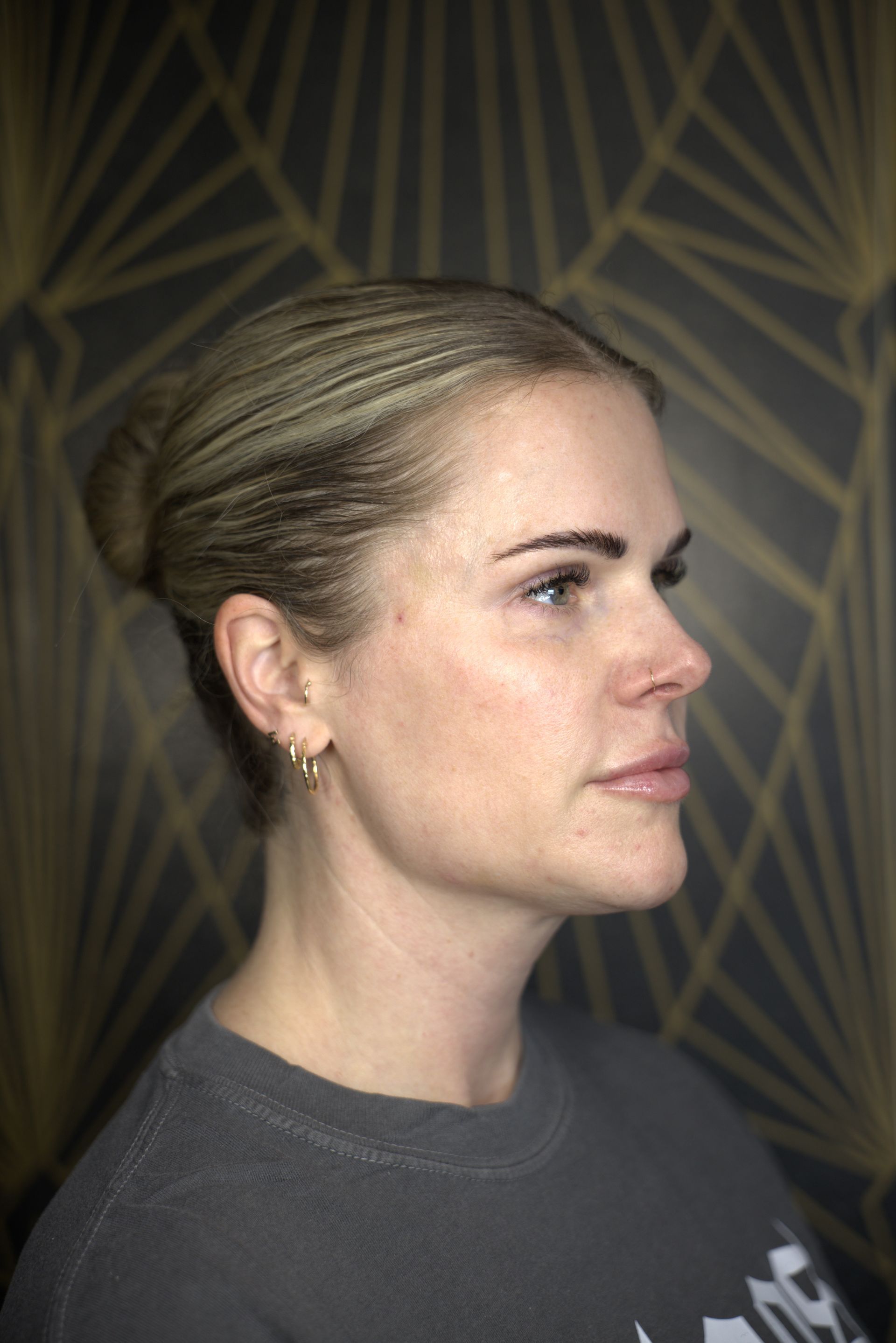 Profile view of a woman with hair in a bun, wearing a dark shirt against a patterned background