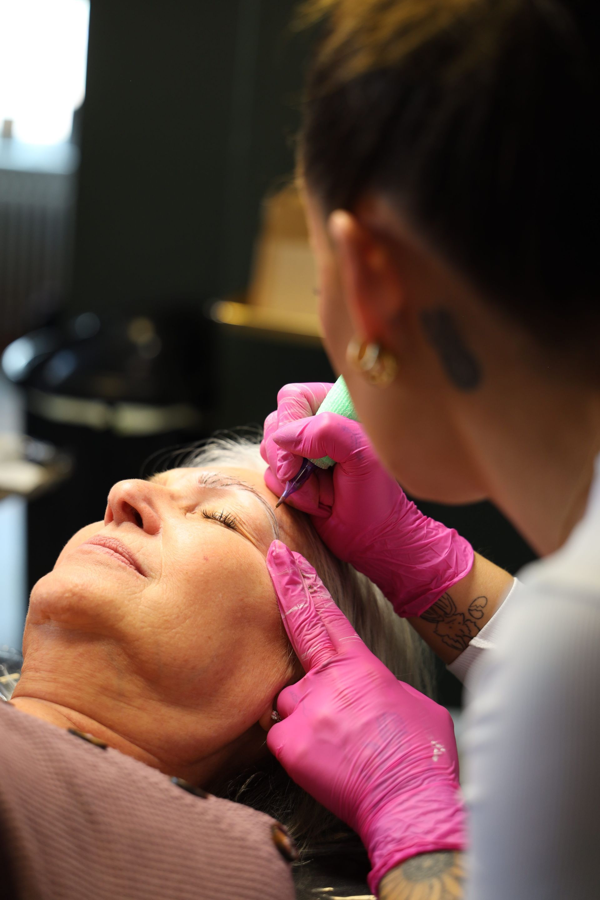 Cosmetic procedure being performed on a client’s eyebrow area by a practitioner wearing pink gloves