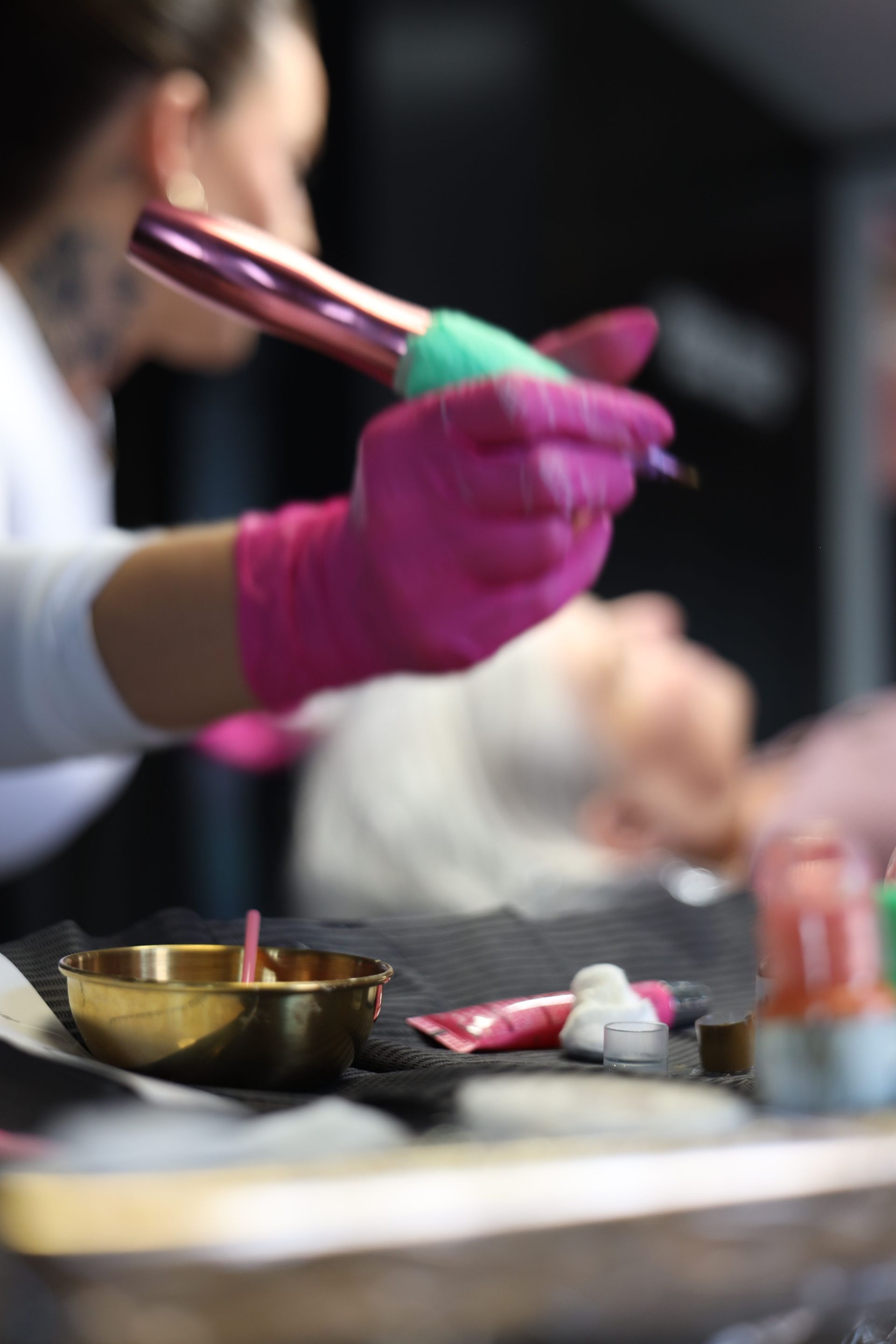 Gloved hands stirring a bowl beside a small brass dish on a table