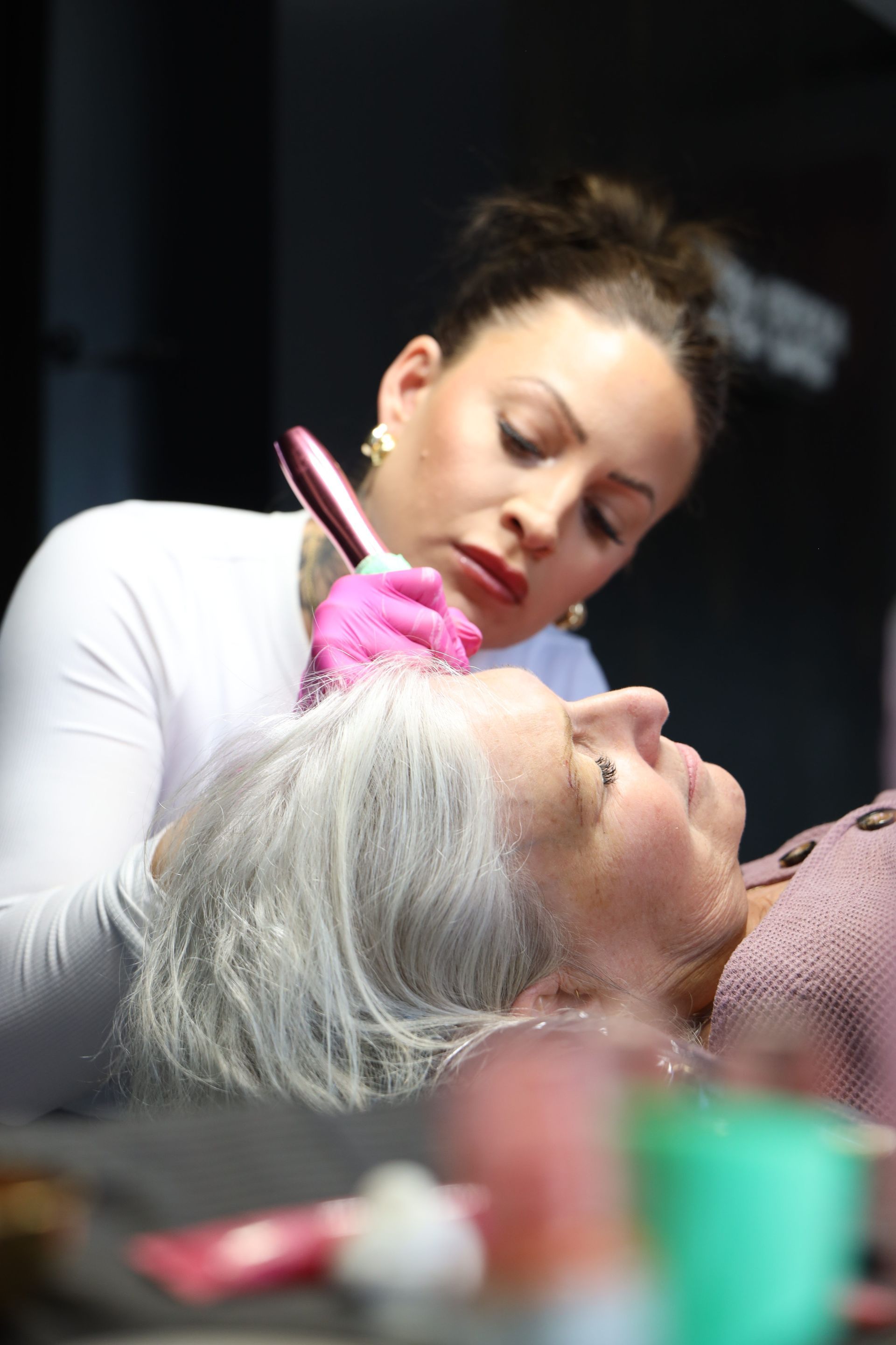 Cosmetologist applying makeup with a brush to a reclining client with white hair