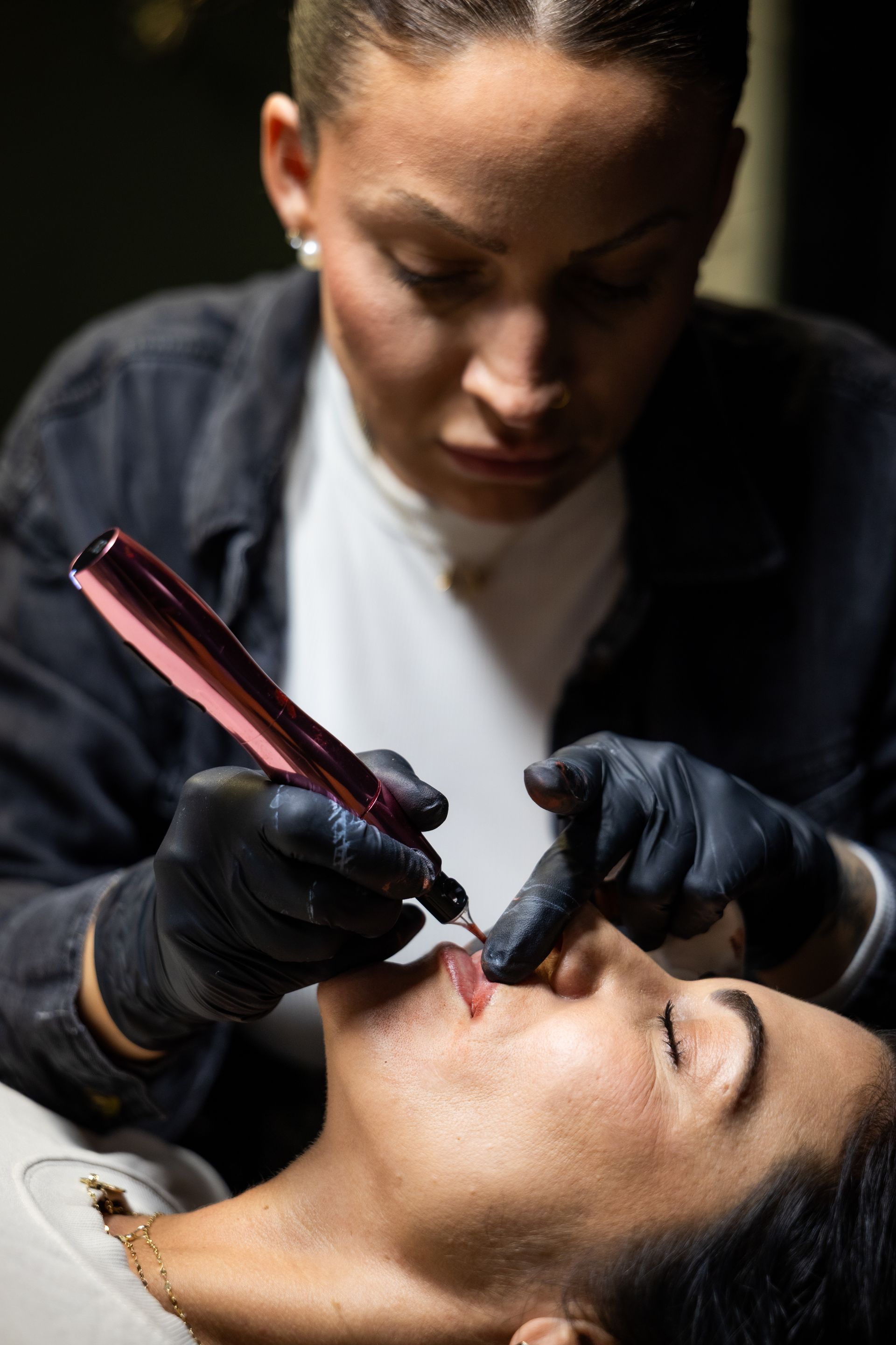 Cosmetologist applying permanent makeup to a client’s eyebrow with a tattoo pen