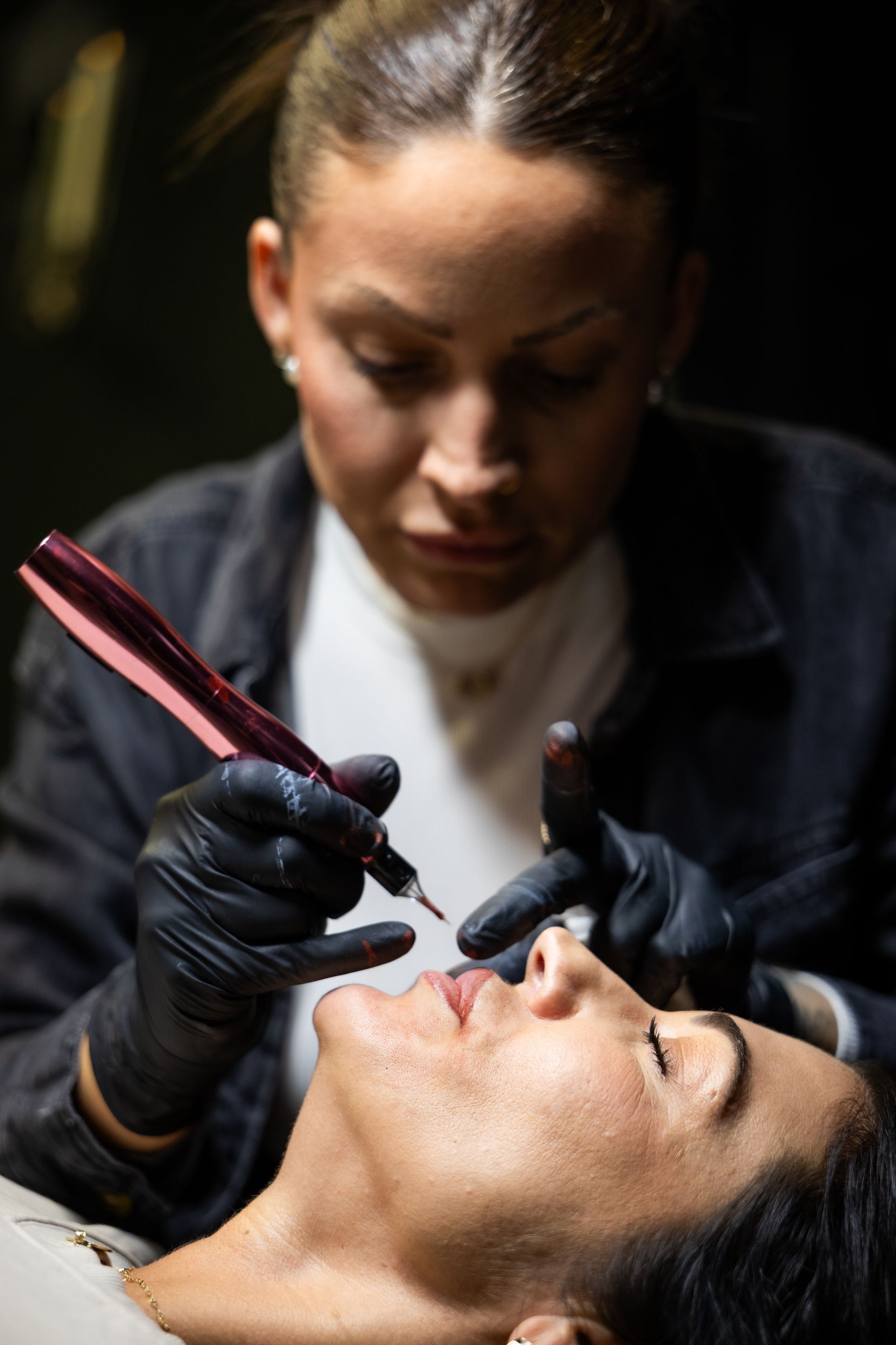 Cosmetologist applying lip pigment to a client with a handheld device during a beauty procedure