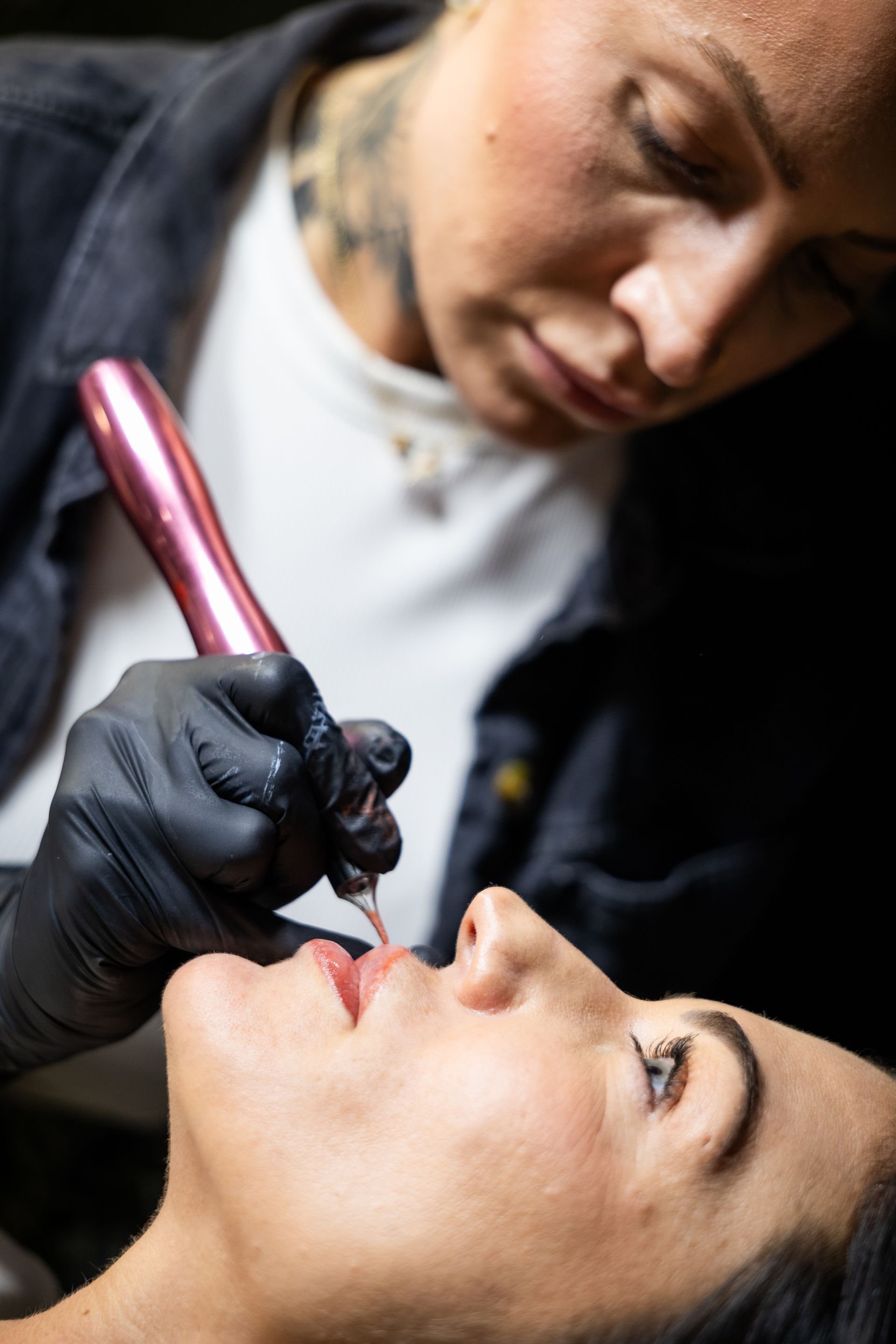 Tattoo artist applying lip color to a client with a pink tool in a close-up salon scene