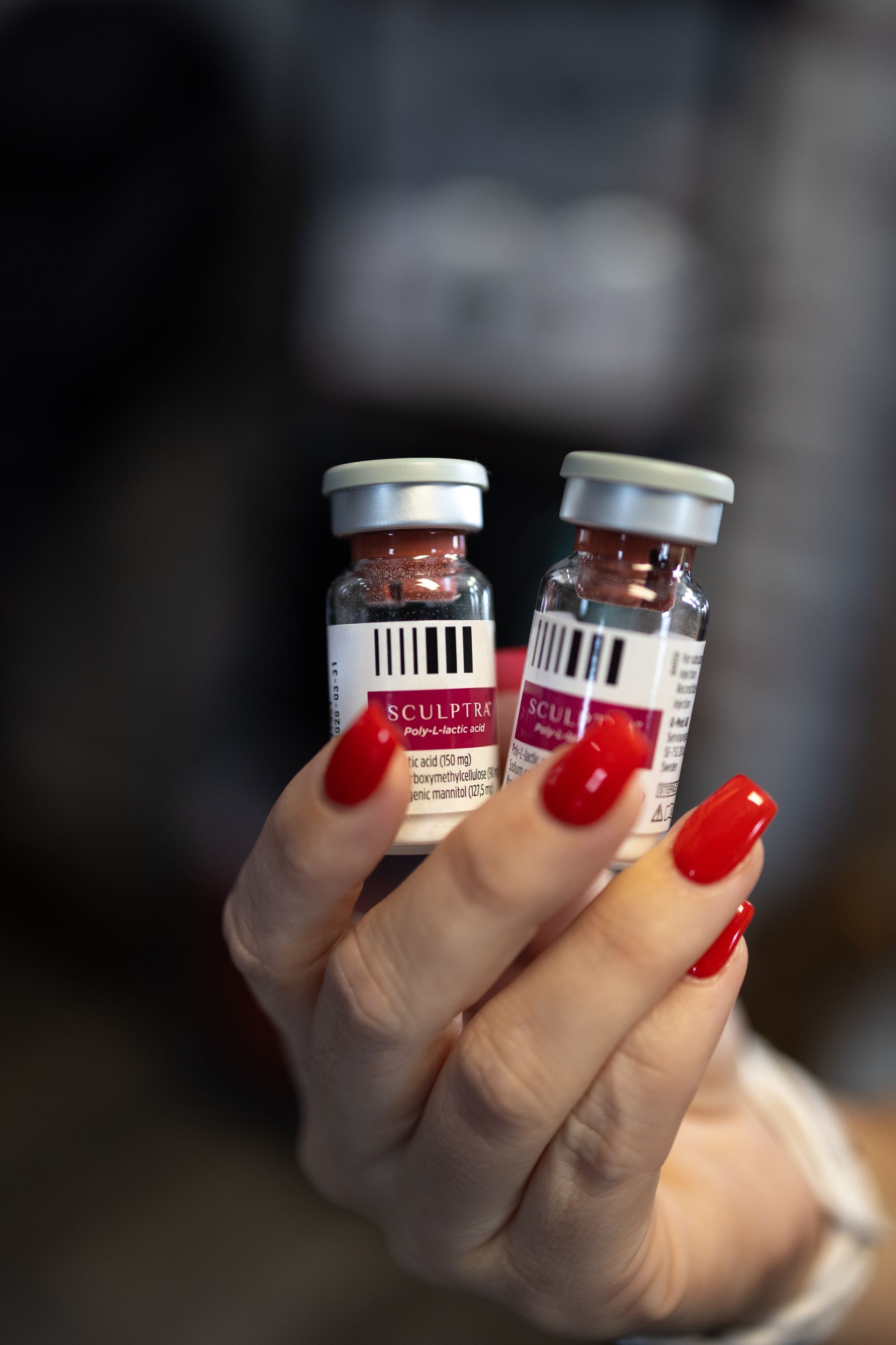 Hand holding two small labeled vials with red caps and red nail polish visible.
