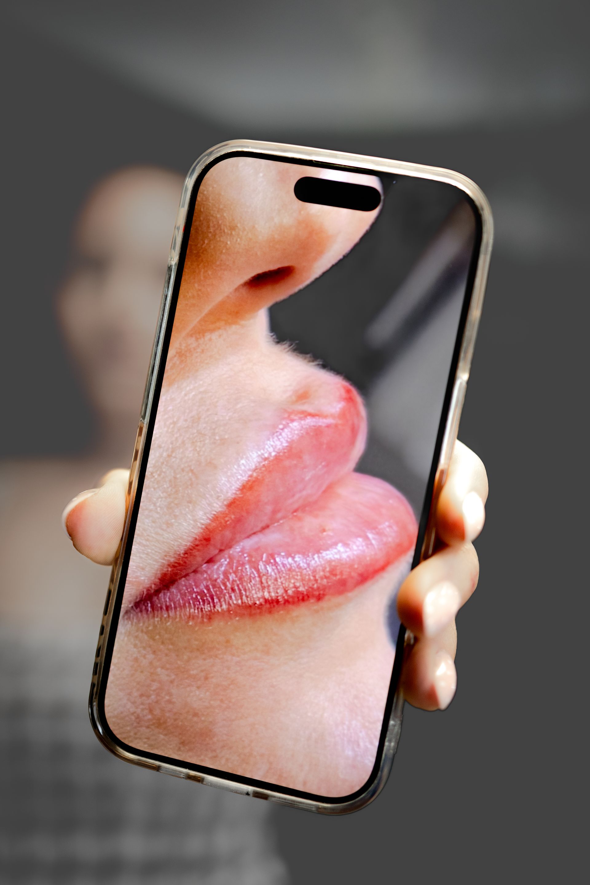 Hand holding a smartphone displaying a close-up of glossy lips and nose