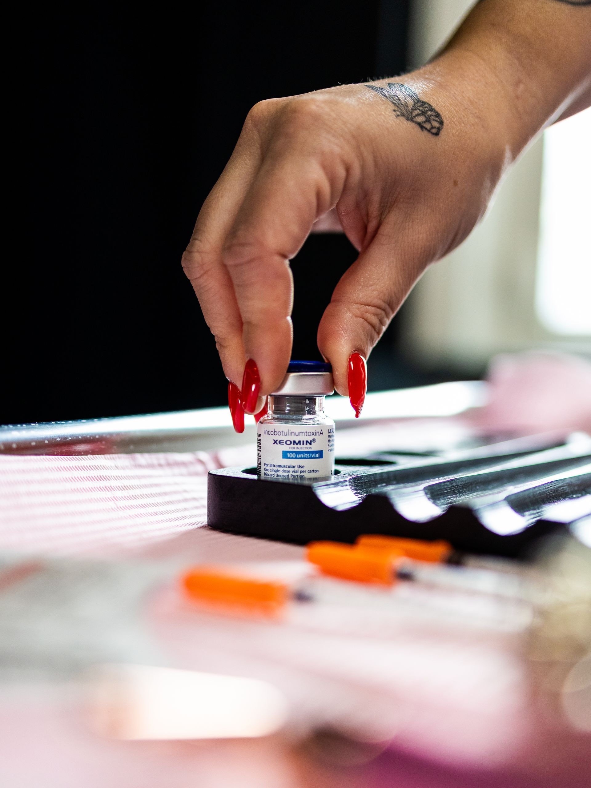 Hand with red nails placing a tiny jar on a table with blurred makeup items in the foreground
