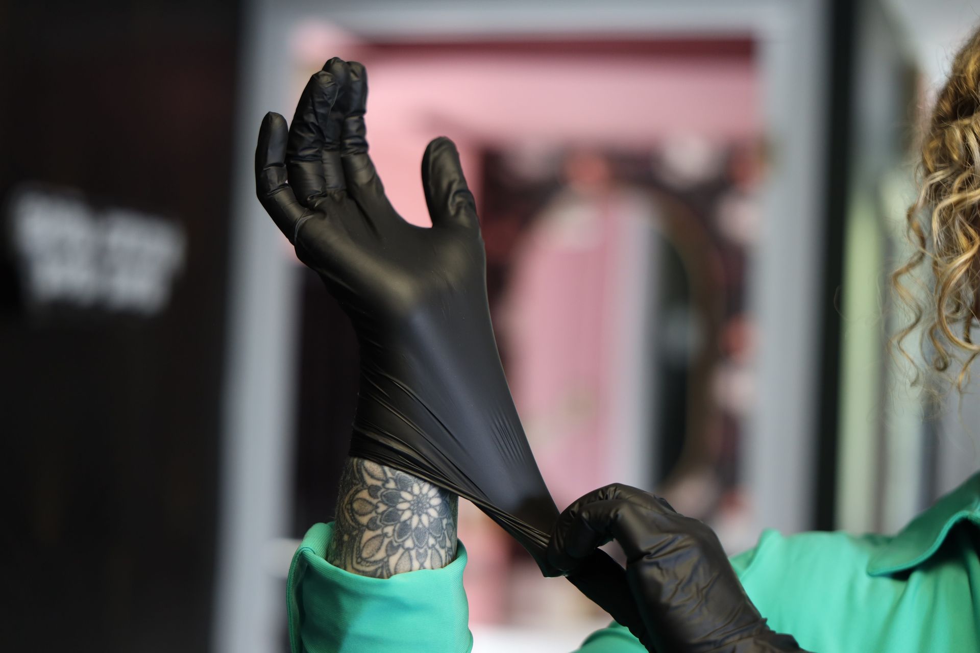 Gloved hands putting on a black glove over a tattooed wrist, with a green sleeve visible.