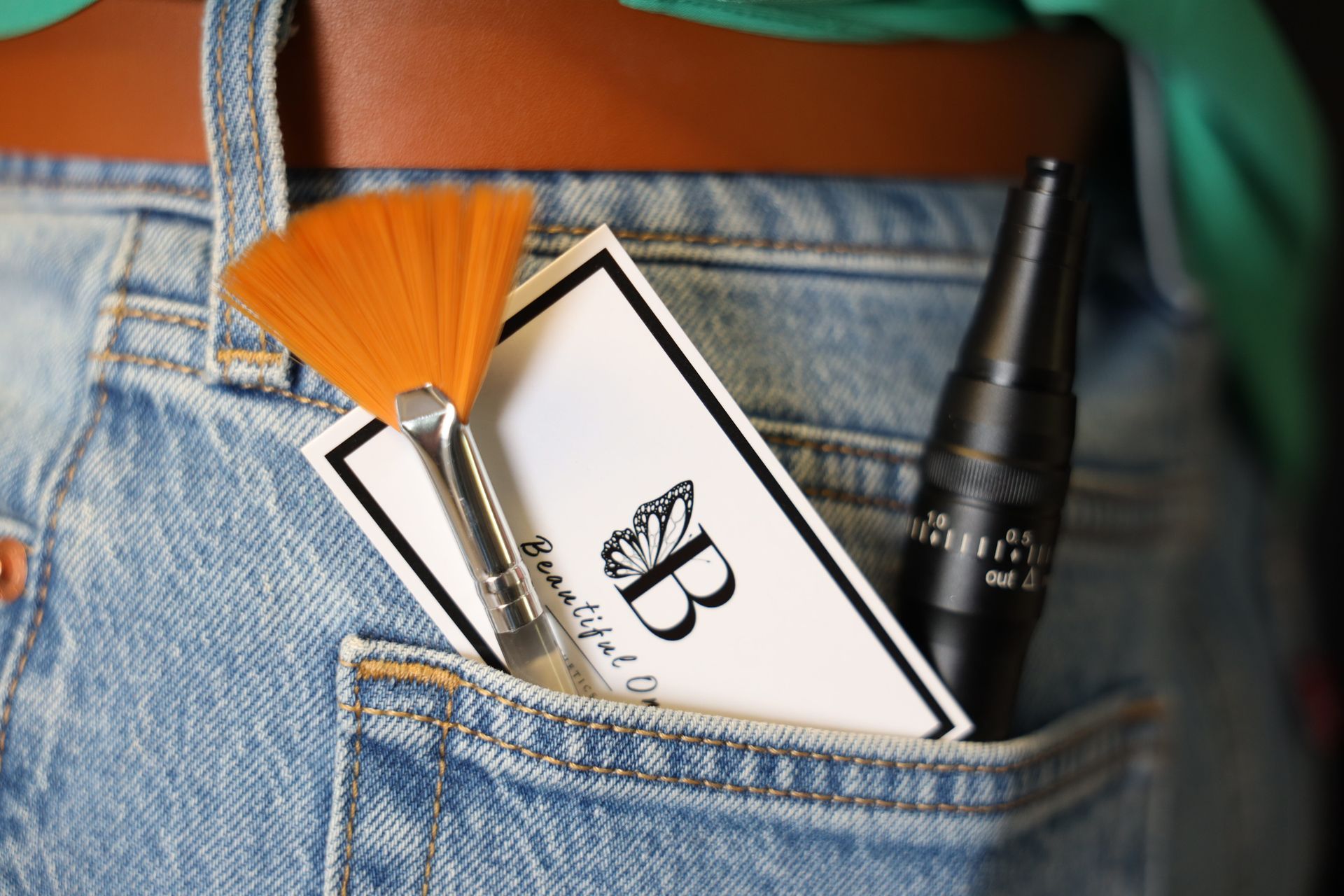 A denim pocket holding a makeup brush, cosmetic card, and black mascara tube.