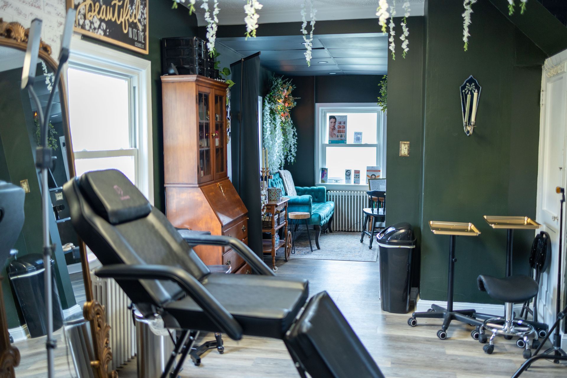 Tattoo studio interior with a black reclining chair, wood cabinets, and a bright window in back.