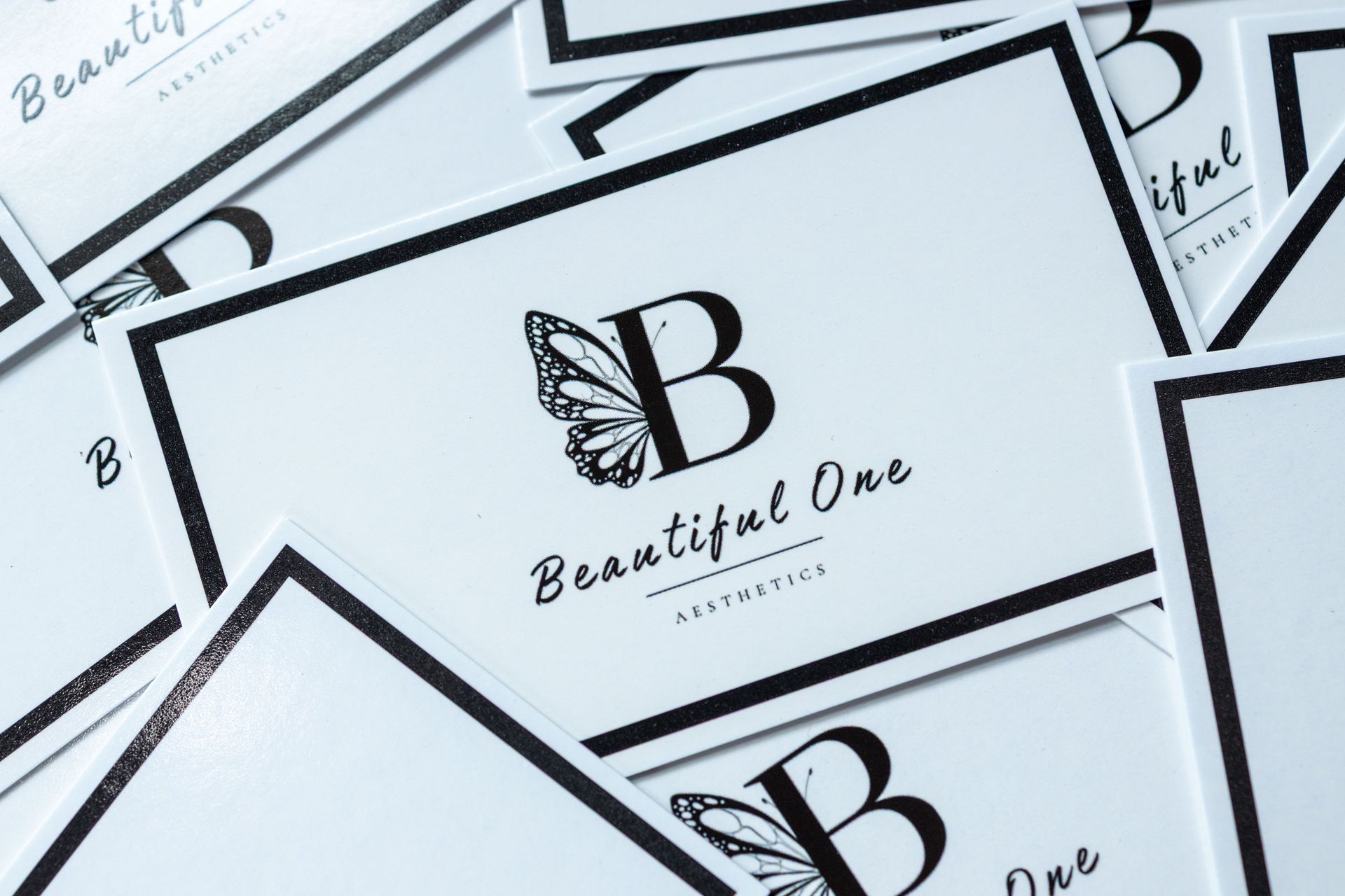 Stack of white business cards with a black butterfly “B” logo and the words “Beautiful One.”