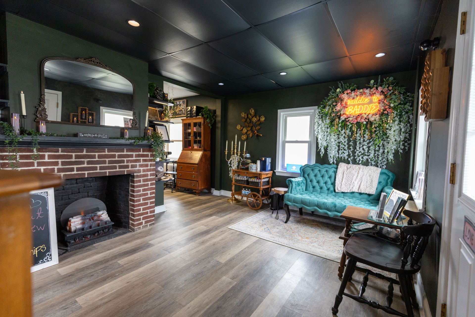 Cozy living room with brick fireplace, teal sofa, dark ceiling, and wood floors