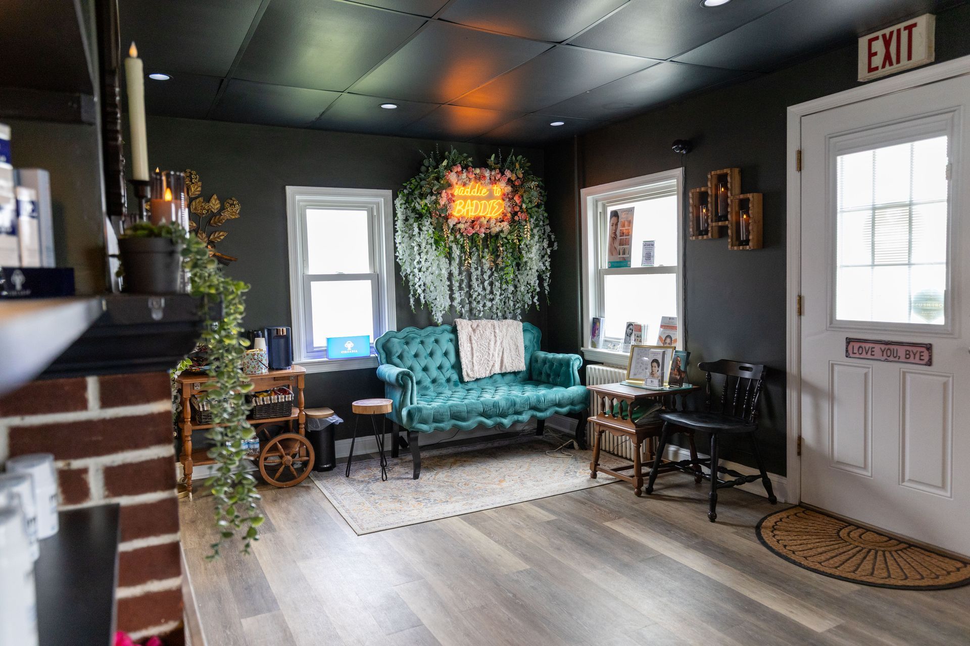 Cozy living room with teal loveseat, dark walls, brick fireplace, and front door with exit sign