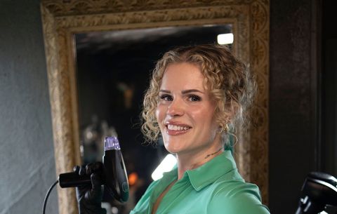 Smiling woman in a green shirt holding a microphone in a dimly lit room