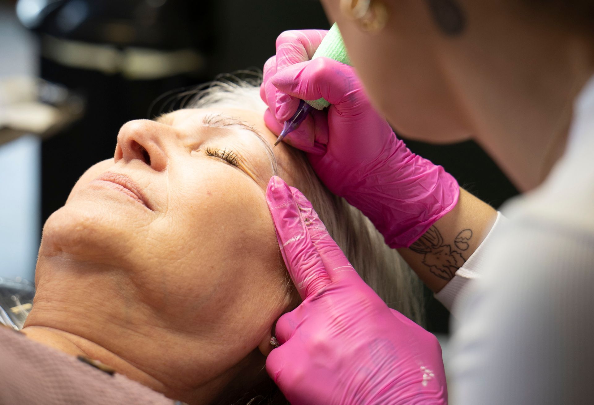 Gloved hands applying a facial treatment to a client lying back with eyes closed