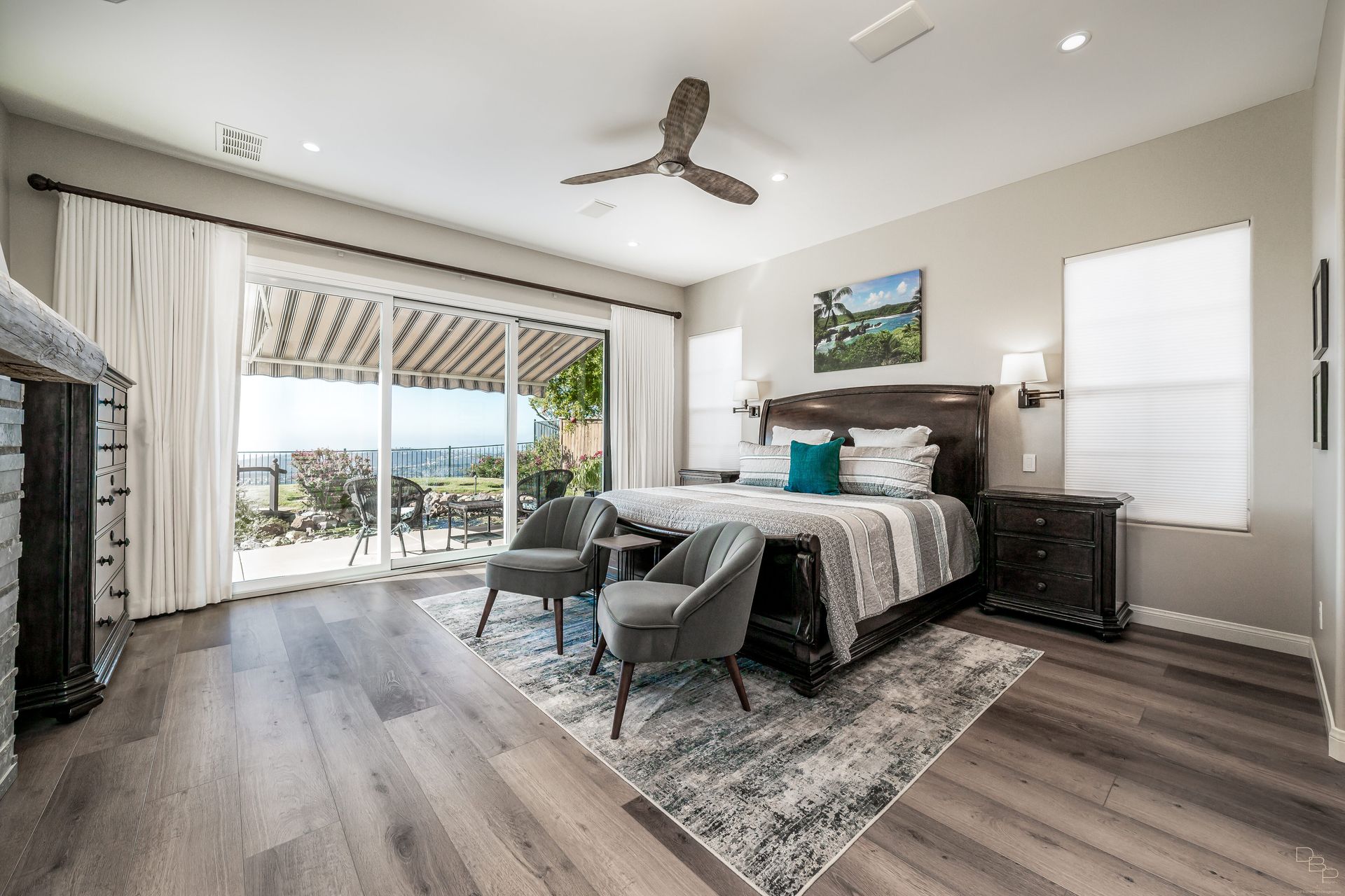 Spacious master bedroom with a king-sized bed, two armchairs, and large sliding doors leading to an outdoor patio with a scenic view.