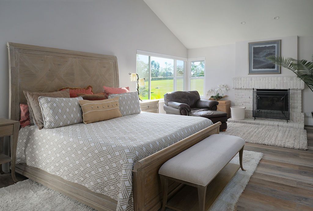 Spacious bedroom with a large bed, a fireplace, and a view of a green lawn through glass doors.