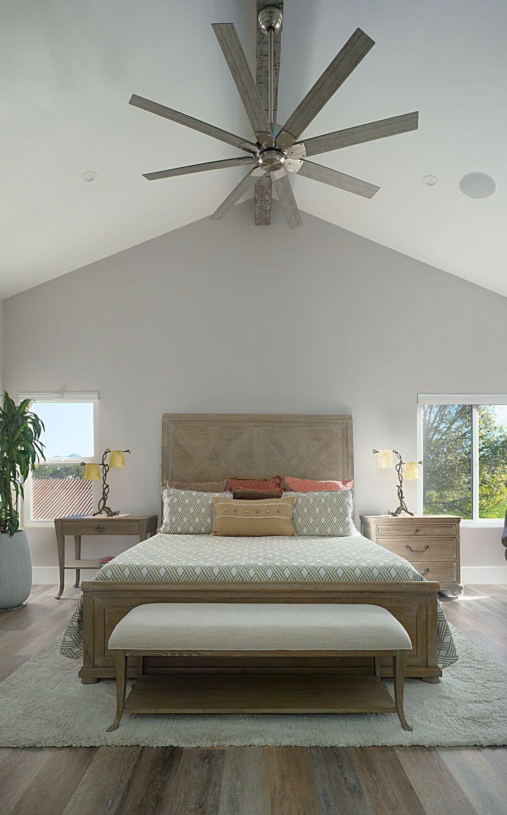 Bedroom with a large bed, bench, and ceiling fan. The room has a vaulted ceiling, neutral colors, and two windows.