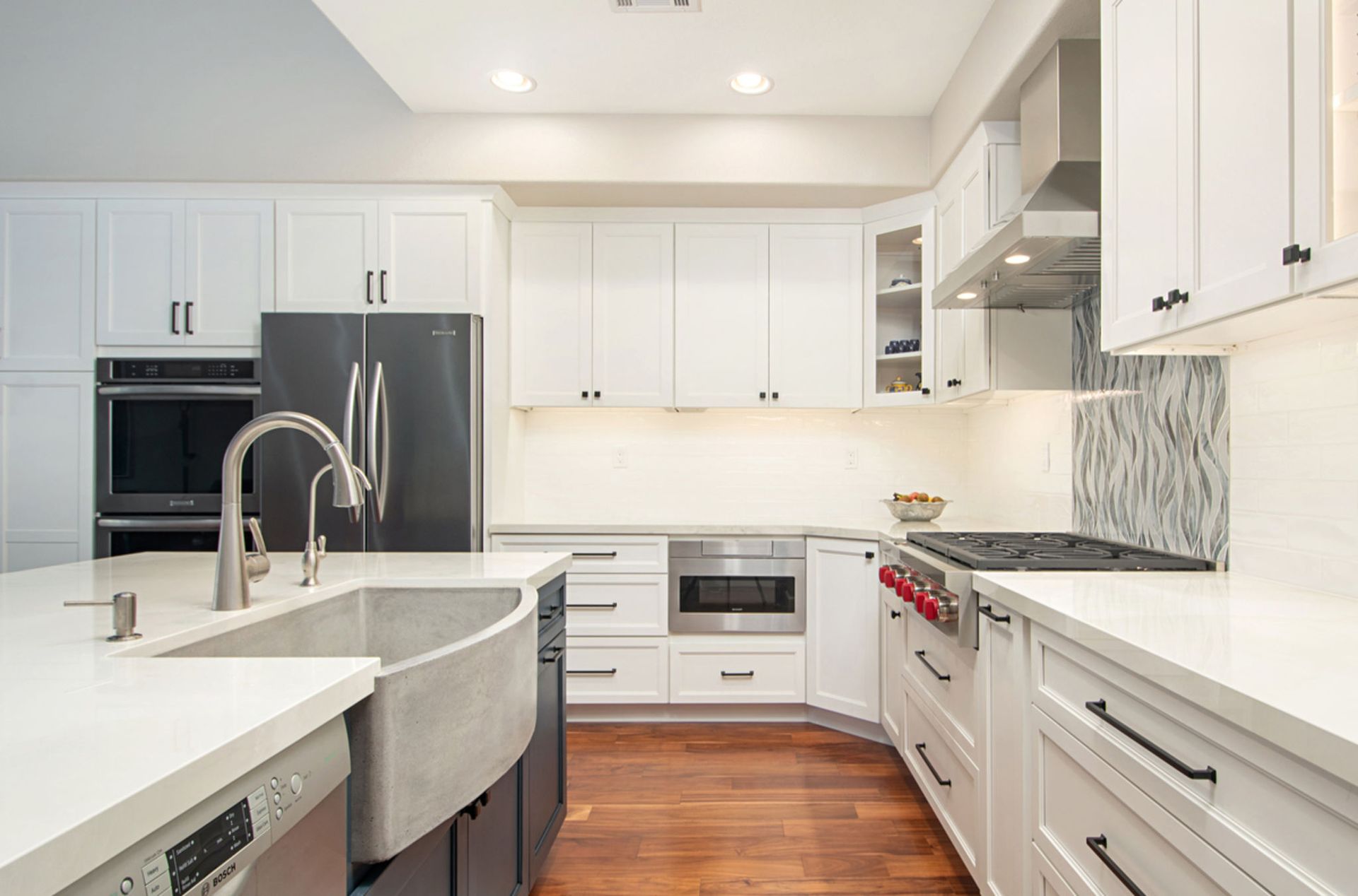 Modern kitchen with white cabinets, dark appliances, a large island, and a stainless steel sink.