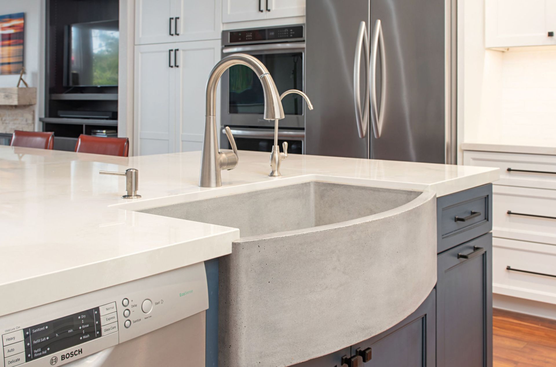 Kitchen island with a gray concrete farmhouse sink, stainless steel faucet, and dishwasher. The cabinetry is blue and white with dark hardware.