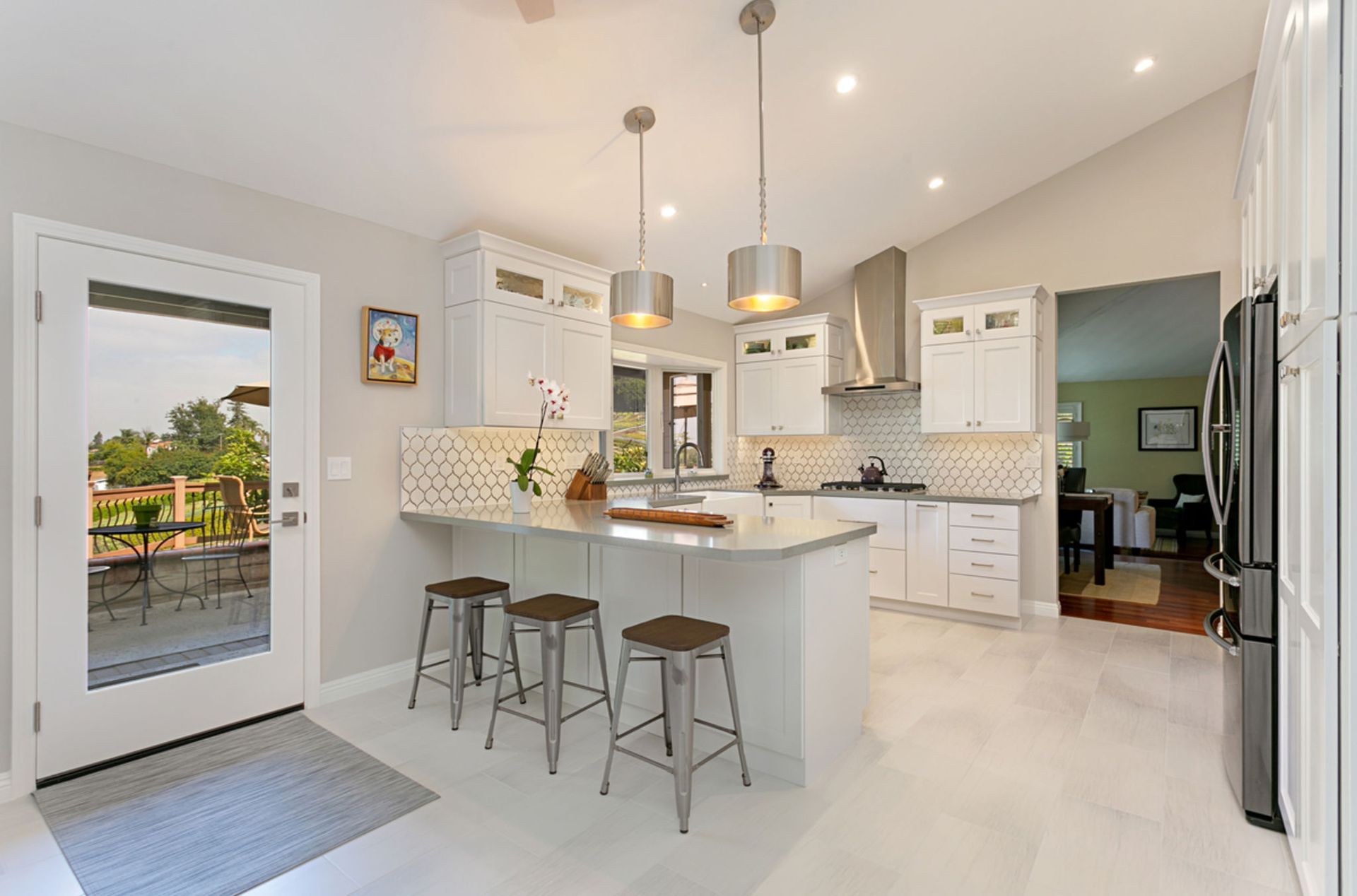 Bright white kitchen with island seating, stainless steel appliances, and a glass door to a patio.