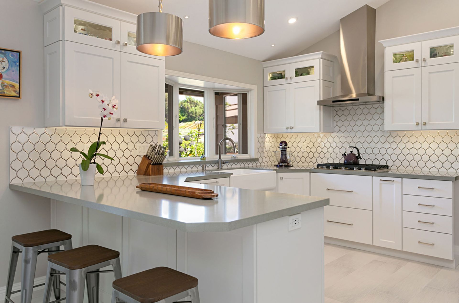 Bright white kitchen with gray countertops, stainless steel appliances, and a breakfast bar with stools.
