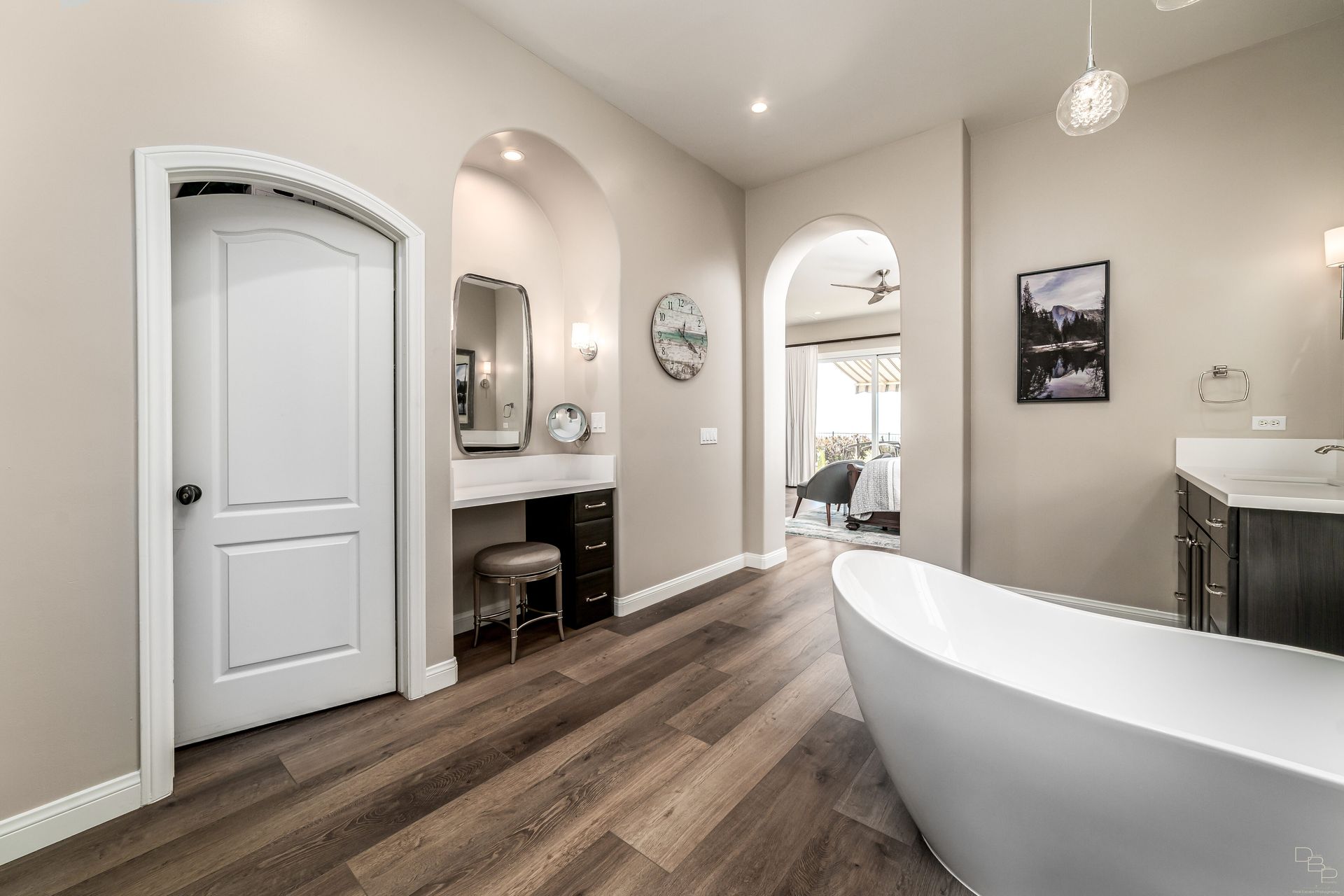 Bathroom with a white freestanding tub, dark wood floors, and a vanity area. A door and arched openings lead to other rooms.
