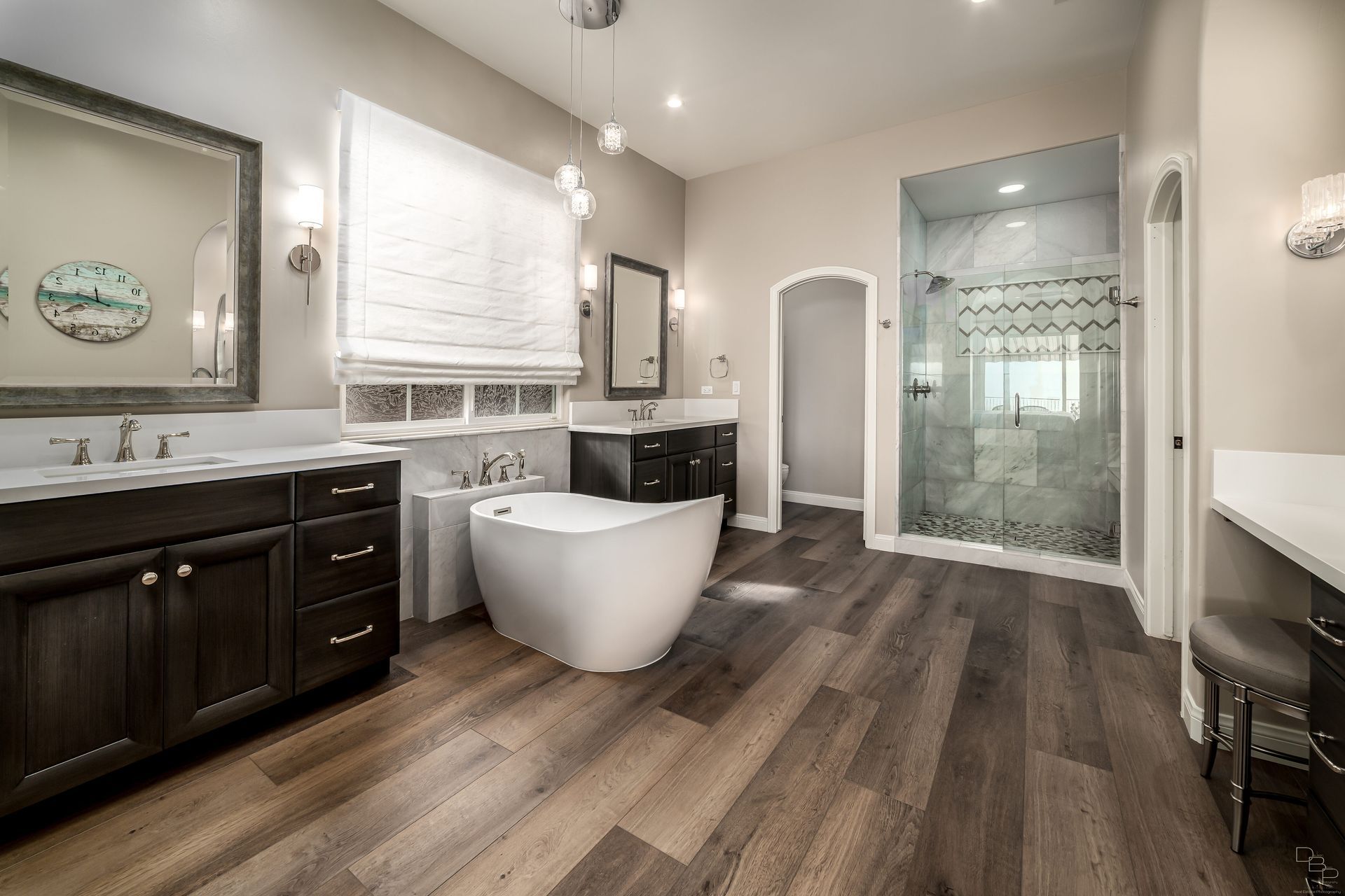 Luxurious bathroom with dark wood floors, a white freestanding tub, dark cabinets, and a glass-enclosed shower.