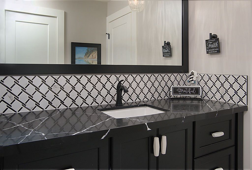 Bathroom vanity with black marble countertop, a white sink, and a patterned tile backsplash. A black framed mirror hangs above.