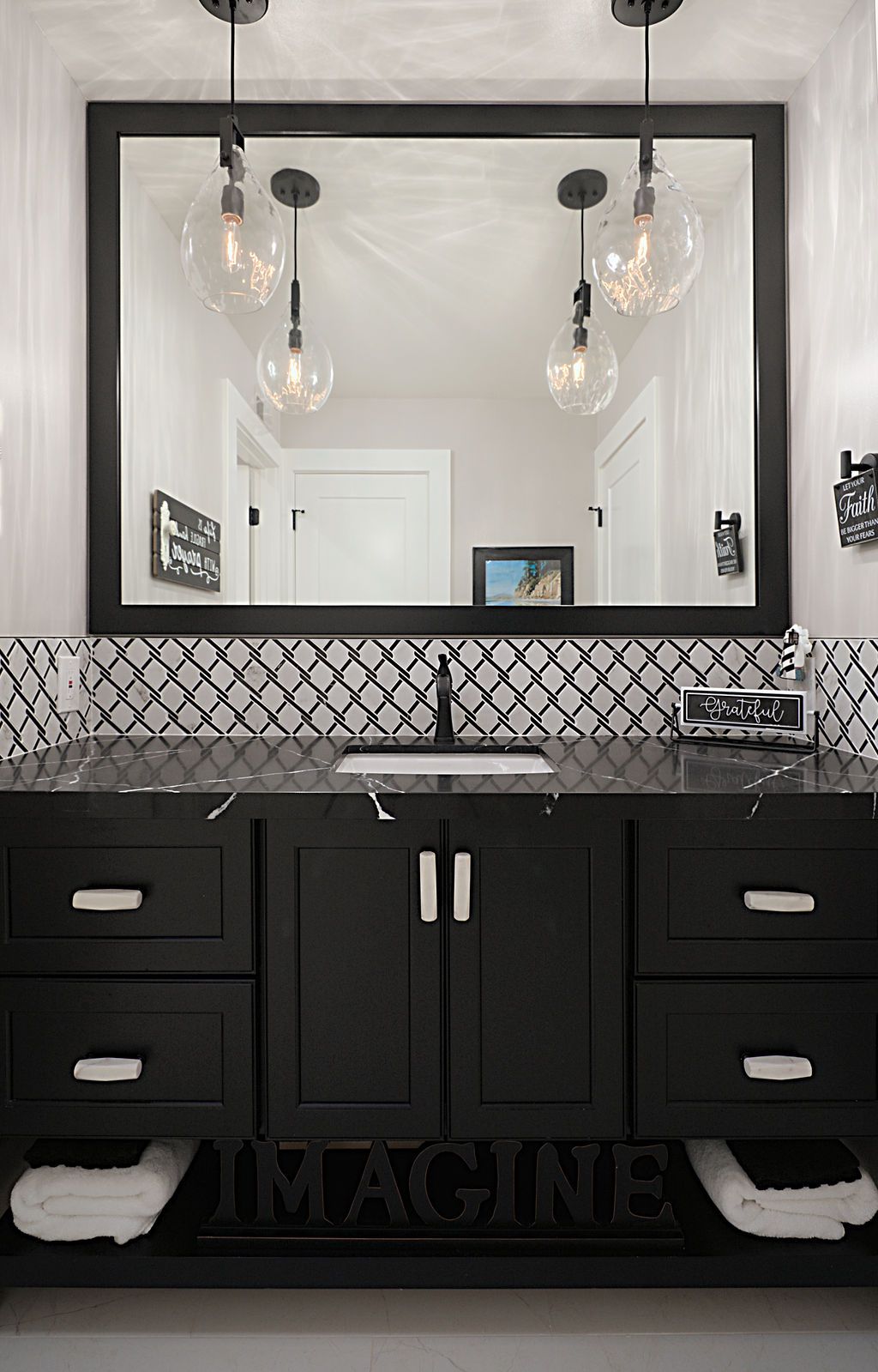 Black vanity with white countertop, black and white backsplash, large mirror, and two pendant lights. The word 