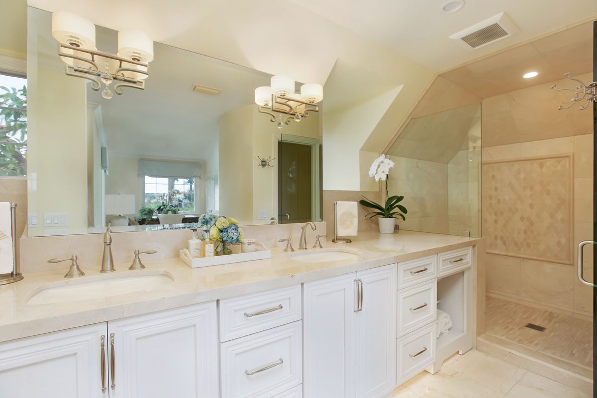 Elegant white bathroom with double sinks, large mirror, and shower. Neutral tones, flower accents.