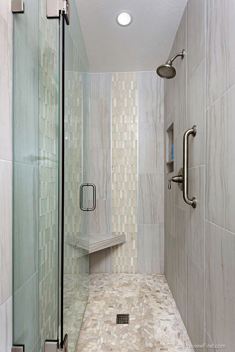 Accessible shower with glass door, gray tiled walls, built-in bench, and grab bar. Light gray mosaic tile accent stripe.