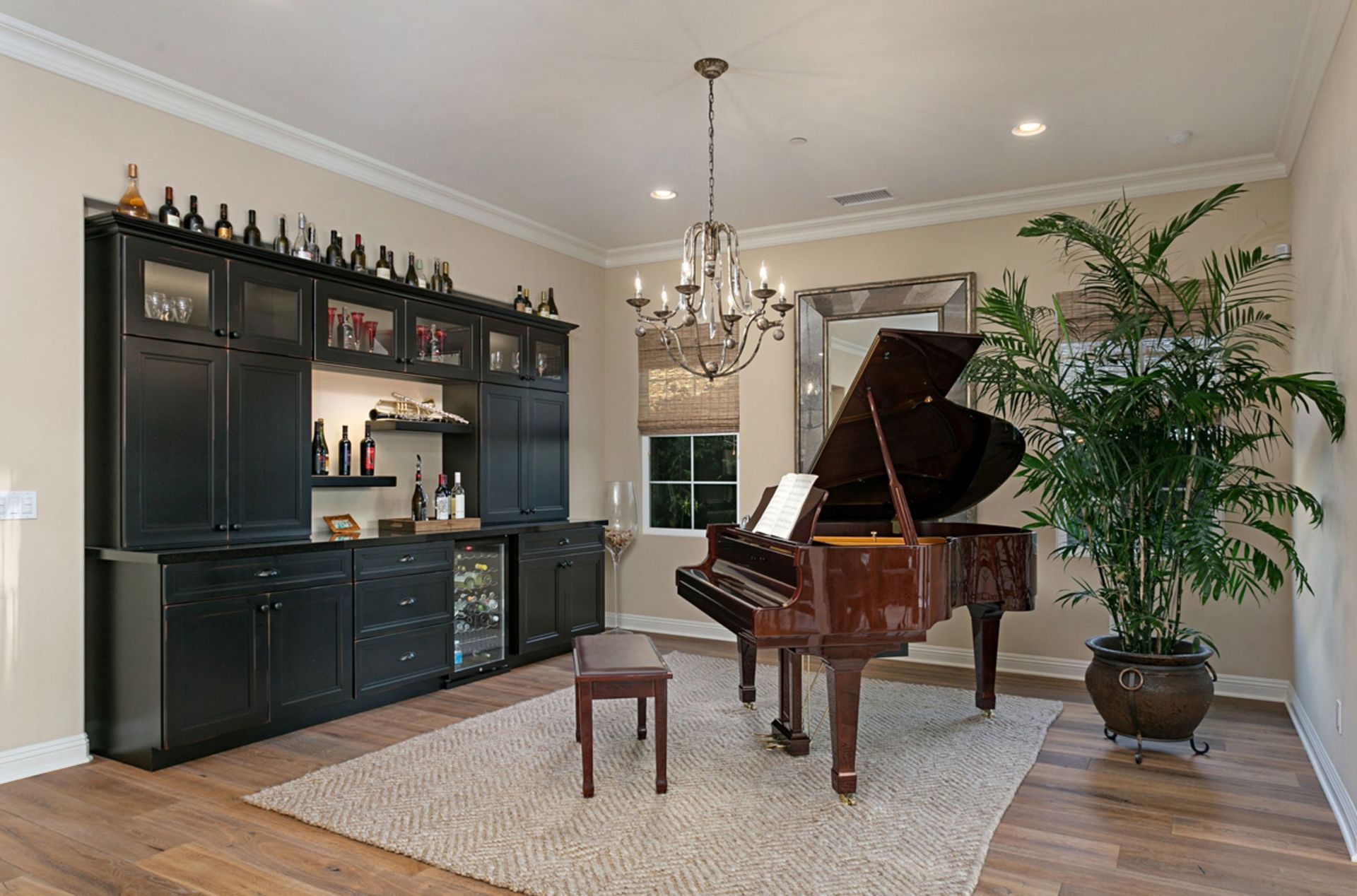 A grand piano in a room with a bar, large mirror, and potted plant. The room has hardwood floors and a chandelier.